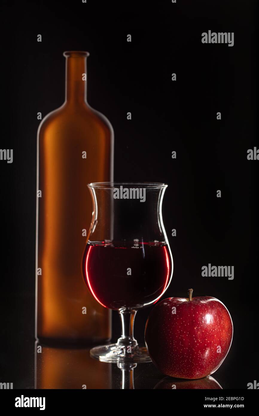 Vetro, bottiglia e mela su fondo nero Foto Stock