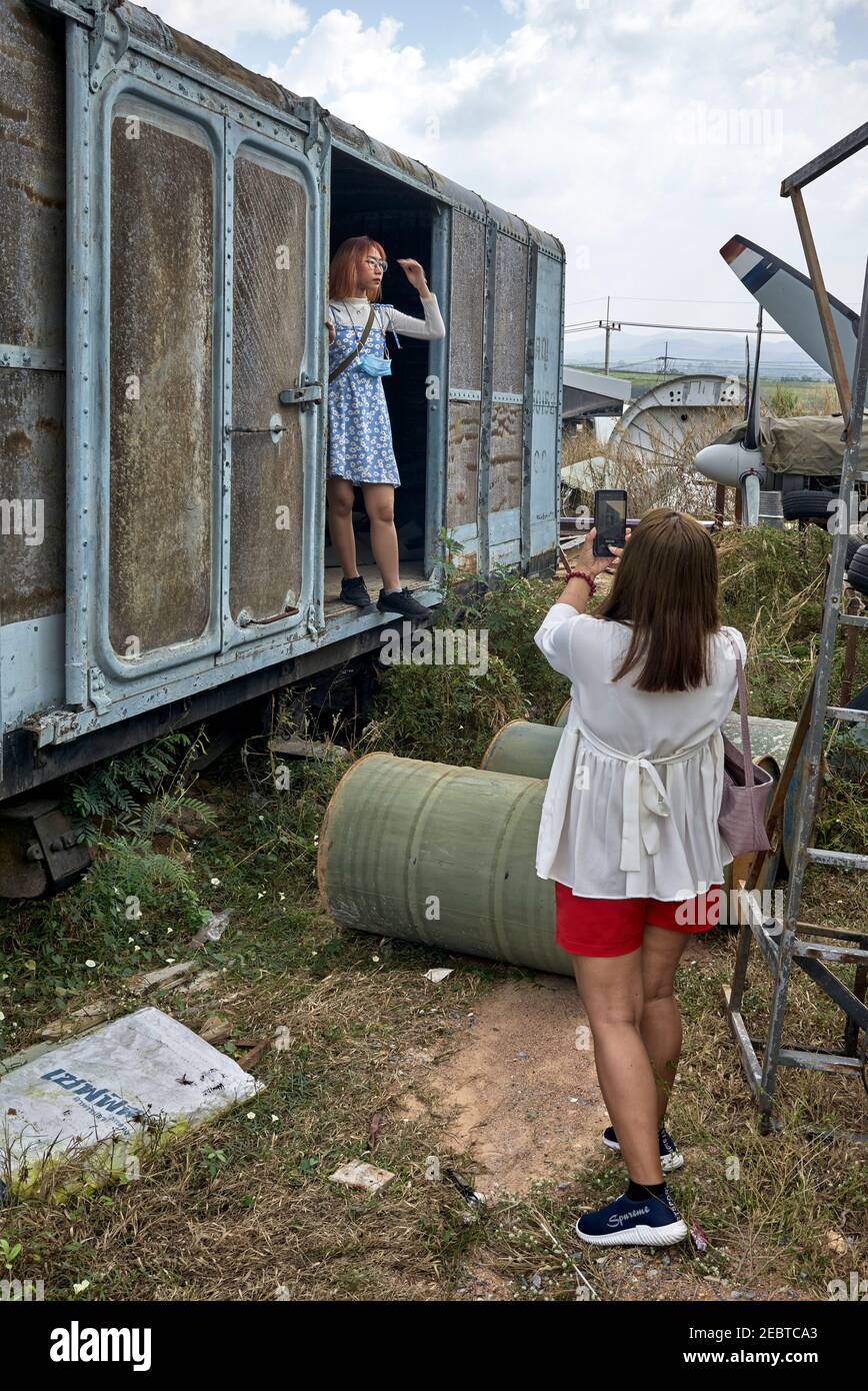 Madre scattando foto di figlia adulta che si posa all'interno di un'arrugginita carrozza ferroviaria d'epoca. Carro merci Foto Stock