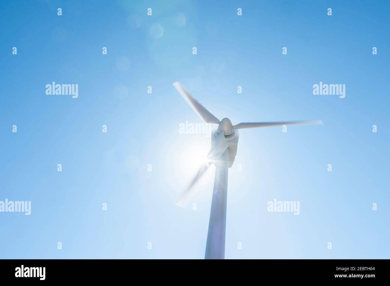 Vista ad angolo basso della turbina eolica contro il cielo blu e. sole Foto Stock