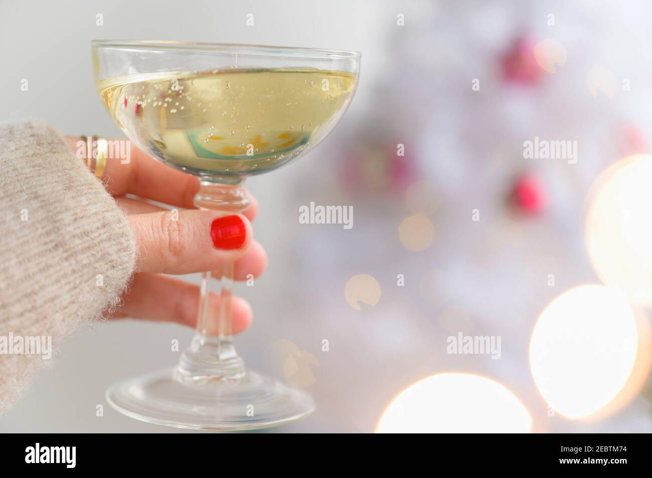 Bicchiere di champagne con mano accanto all'albero di Natale Foto Stock