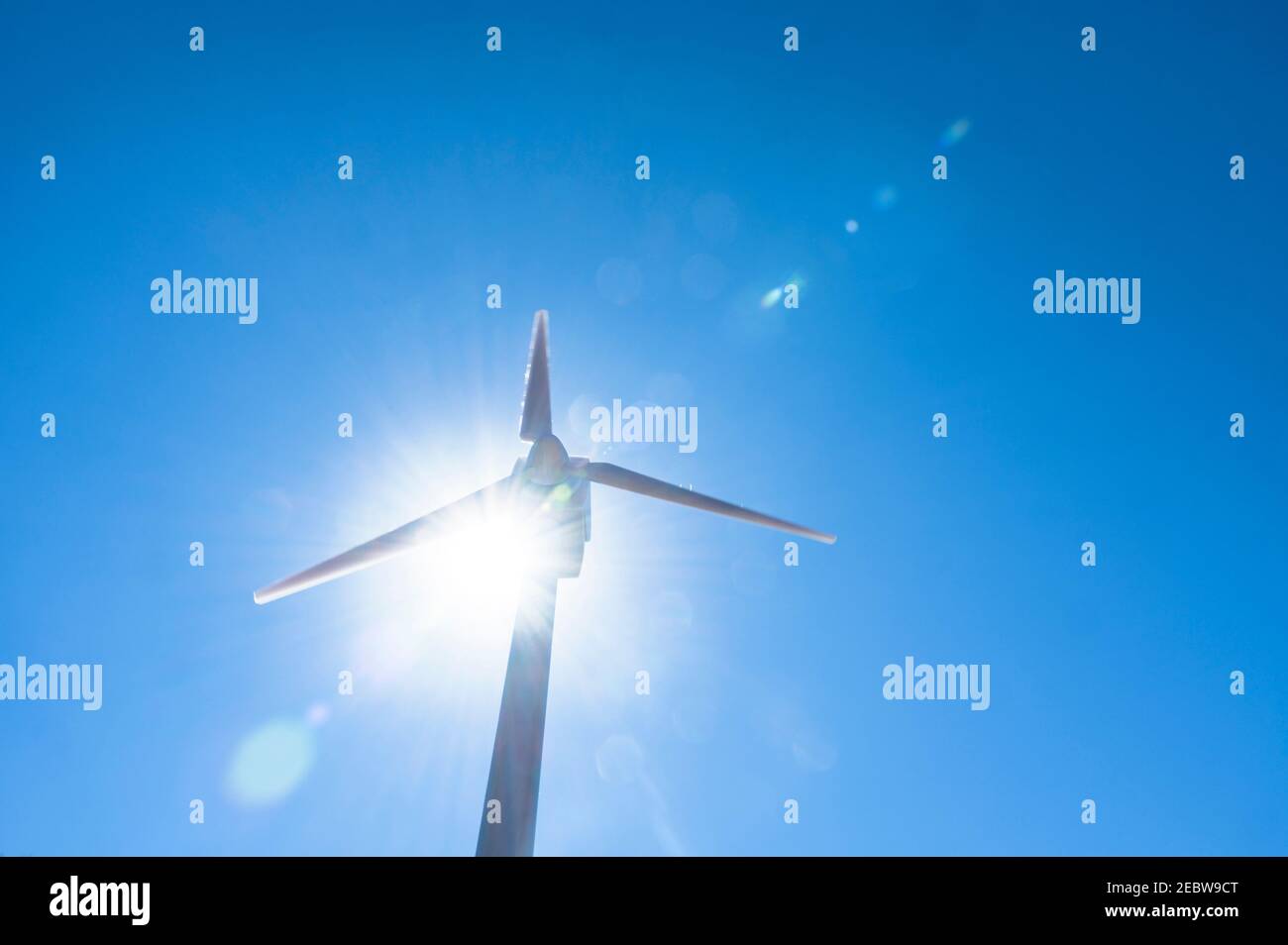 Vista ad angolo basso della turbina eolica contro il cielo blu e. sole Foto Stock