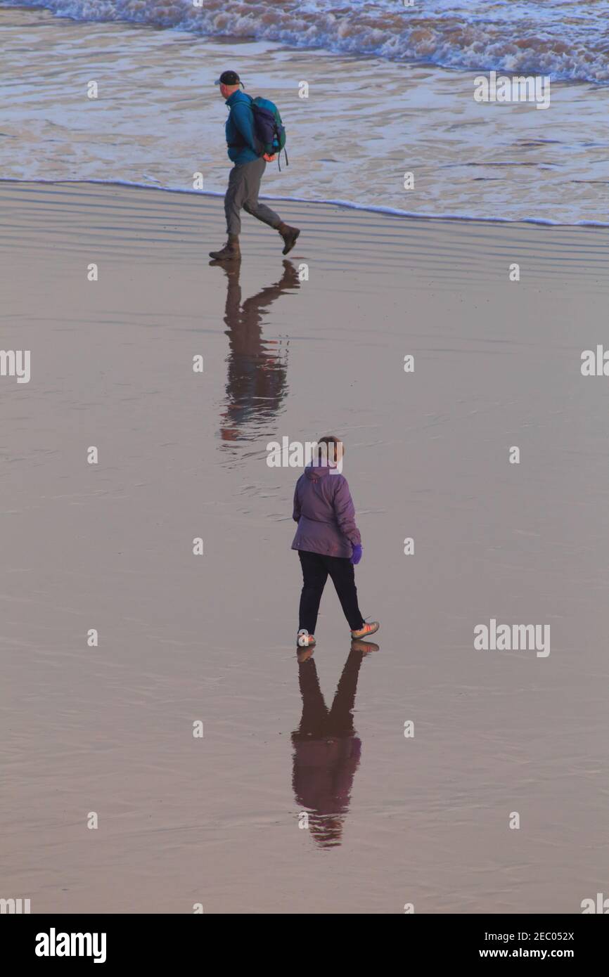 La gente cammina sulla spiaggia di sabbia nella città di Sidmouth, Devon. Riflessione sulla superficie dell'acqua. Foto Stock