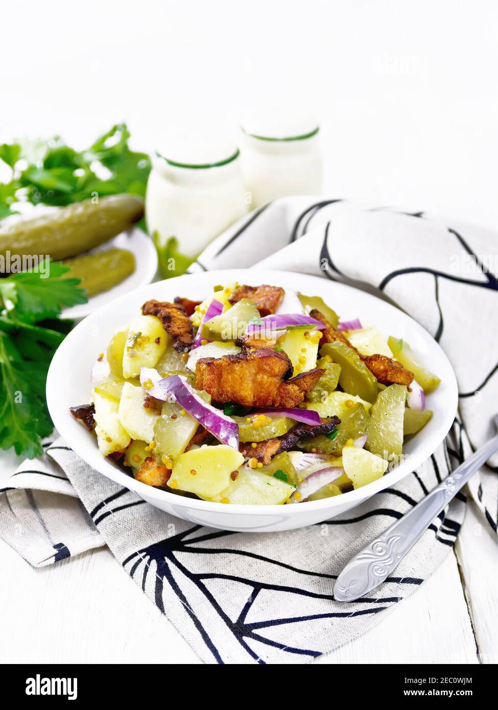 Insalata di patate bollite, pancetta fritta, cipolla rossa e cetrioli sottaceto, condita con senape di grano, spezie e olio vegetale in un piatto su tovagliolo agai Foto Stock