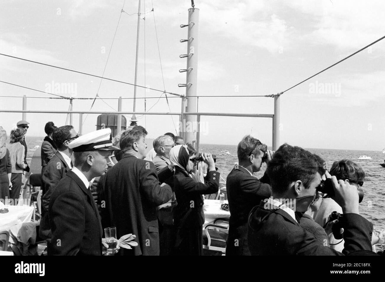 Il presidente Kennedy si accuda alla prima gara di Coppa Americau0027s. Il presidente John F. Kennedy e la First Lady Jacqueline Kennedy (entrambi guardando attraverso il binocolo) guardano la prima gara della Coppa Americau0027s 1962 a bordo della USS Joseph P. Kennedy, Jr. Anche nella foto: Capo del protocollo, Angier Biddle Duke; Julia Ann Shepard (moglie di Aide Navale al presidente, Capitano Tazewell Shepard); skipper dello yacht presidenziale, u201cManitou,u201d tenente Charles Reid; Franklin D. Roosevelt, Jr.; Hugh D. Auchincloss; Jamie Auchincloss; Janet Jennings Auchincloss. Newport, Rhode Island. Foto Stock