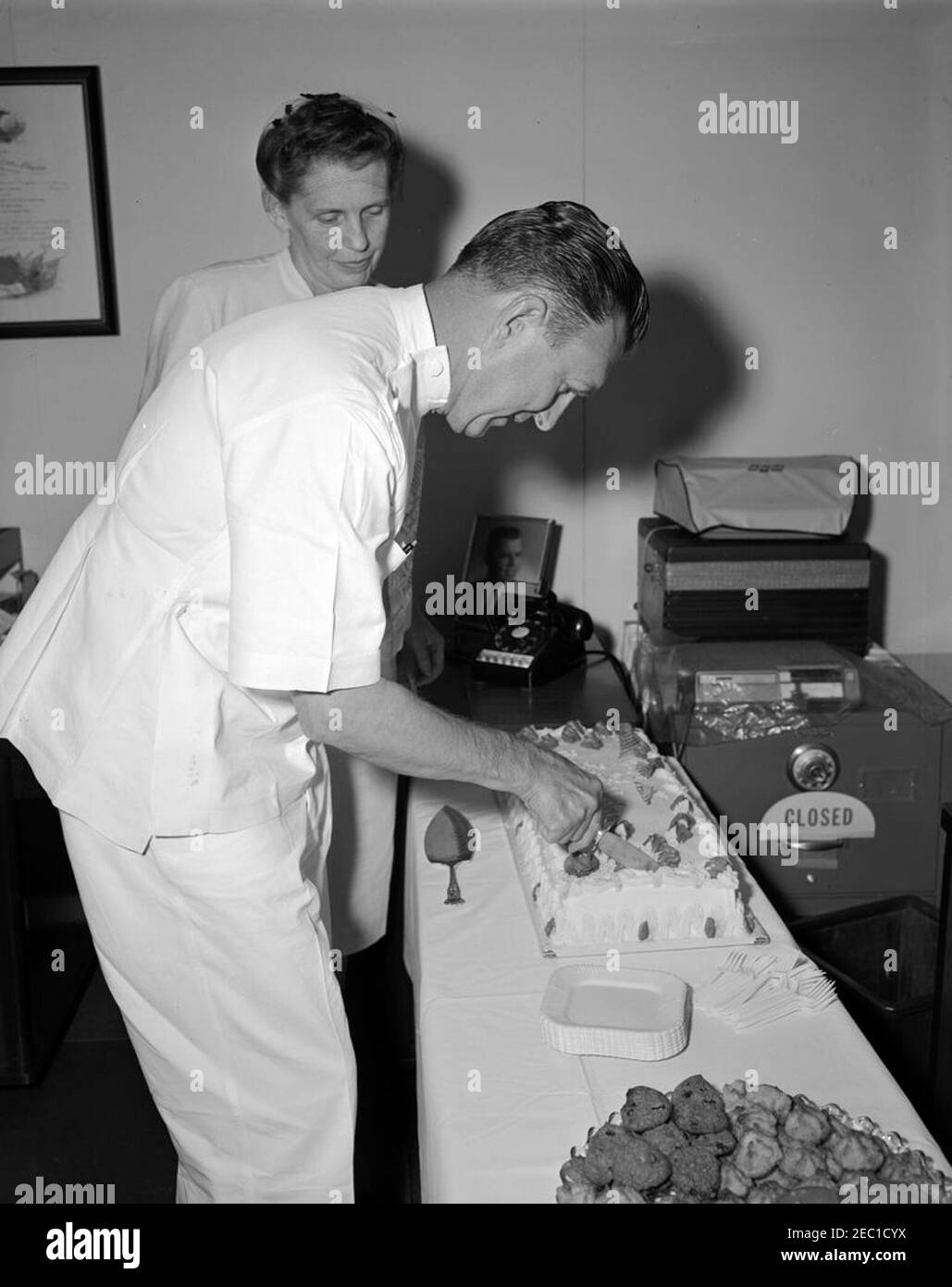 Partito di pensionamento, il Lt. Colonnello Philip Sidmore, presidente Kennedyu2019s Phyicianu2019s Ufficio. Il tenente colonnello Philip Sidmore, dell'ufficio del presidente John F. Kennedyu0027s medico, taglia la torta al suo partito di pensione. Dietro si erge la moglie del Lt. Colon. Sidmoreu2019, Alada Sidmore. White House, Washington, D.C. [fotografia di Dan Lewis] Foto Stock