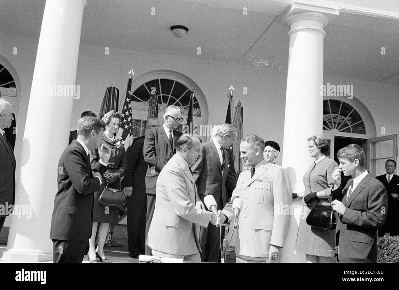 Cerimonia di giuramento, Gen. Maxwell Taylor, Presidente, JCS, 12:00. Presidente appena nominato dei Capi congiunti del personale (JCS), generale Maxwell D. Taylor (centro destra), stringe le mani con il presidente uscente del JCS, generale Lyman L. Lemnitzer, dopo la cerimonia di giuramento nel Rose Garden della Casa Bianca, Washington, D.C. guardando (da sinistra a destra): Generale Omar Bradley; Il presidente John F. Kennedy; Lydia Taylor; il capo delle operazioni navali, l'ammiraglio George W. Anderson, Jr. (In dietro, parzialmente nascosto); il segretario della Marina, Fred Korth; il segretario aggiunto della difesa, Roswell Gilpatric; P. Foto Stock