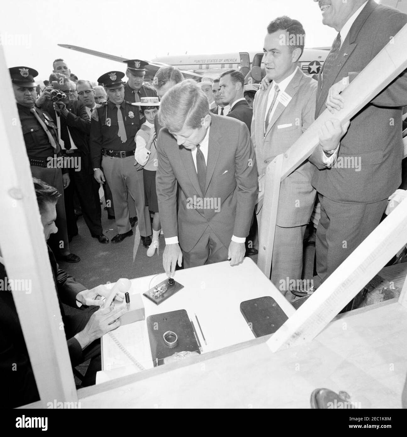 Viaggio della campagna del Congresso: Muskegon, Michigan, discorso all'aeroporto, cerimonia di apertura di un incontro massonico a Chicago. Il presidente John F. Kennedy si prepara a premere un pulsante per inaugurare un incontro massonico a Chicago, Illinois, durante un viaggio di campagna al Congresso all'aeroporto della contea di Muskegon, Michigan. Anche nella foto: Candidato al Congresso del Michigan, Neil Staebler (a destra, parzialmente fuori dal quadro); fotografo di newsreel per United Press Movietone, Thomas J. Craven, Sr.; funzionario della White House Communications Agency (WHCA), Joe Taylor; agenti della White House Secret Service, Walt Co Foto Stock