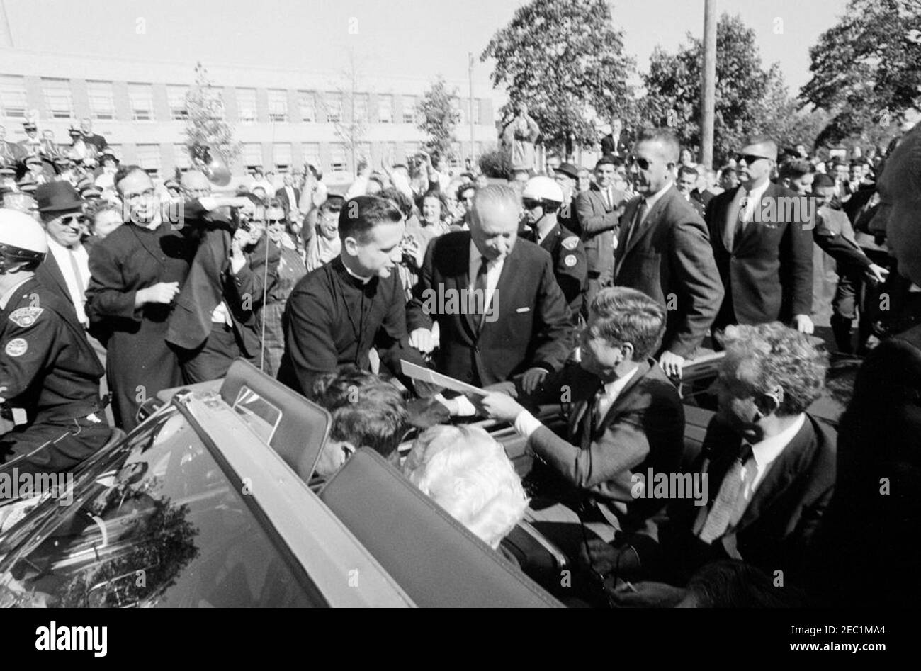 Viaggio della campagna del Congresso: Cleveland, Ohio, arrivo, rally, moto, partenza. Il presidente John F. Kennedyu2019s si ferma di fronte alla St. Edward High School a Lakewood, Ohio, durante un viaggio di campagna del Congresso; il presidente Kennedy scuote le mani con il direttore, Fratel Charles Krupp. Anche nella foto: Il rappresentante Michael J. Feighan dell'Ohio (davanti al sedile convertibile, indietro alla telecamera); il senatore Frank Lausche dell'Ohio (in sedile posteriore con il presidente Kennedy); il governatore dell'Ohio, Michael V. DiSalle (in piedi all'estrema destra in primo piano); il fratello Florentius Schu (in piedi a sinistra sullo sfondo Foto Stock