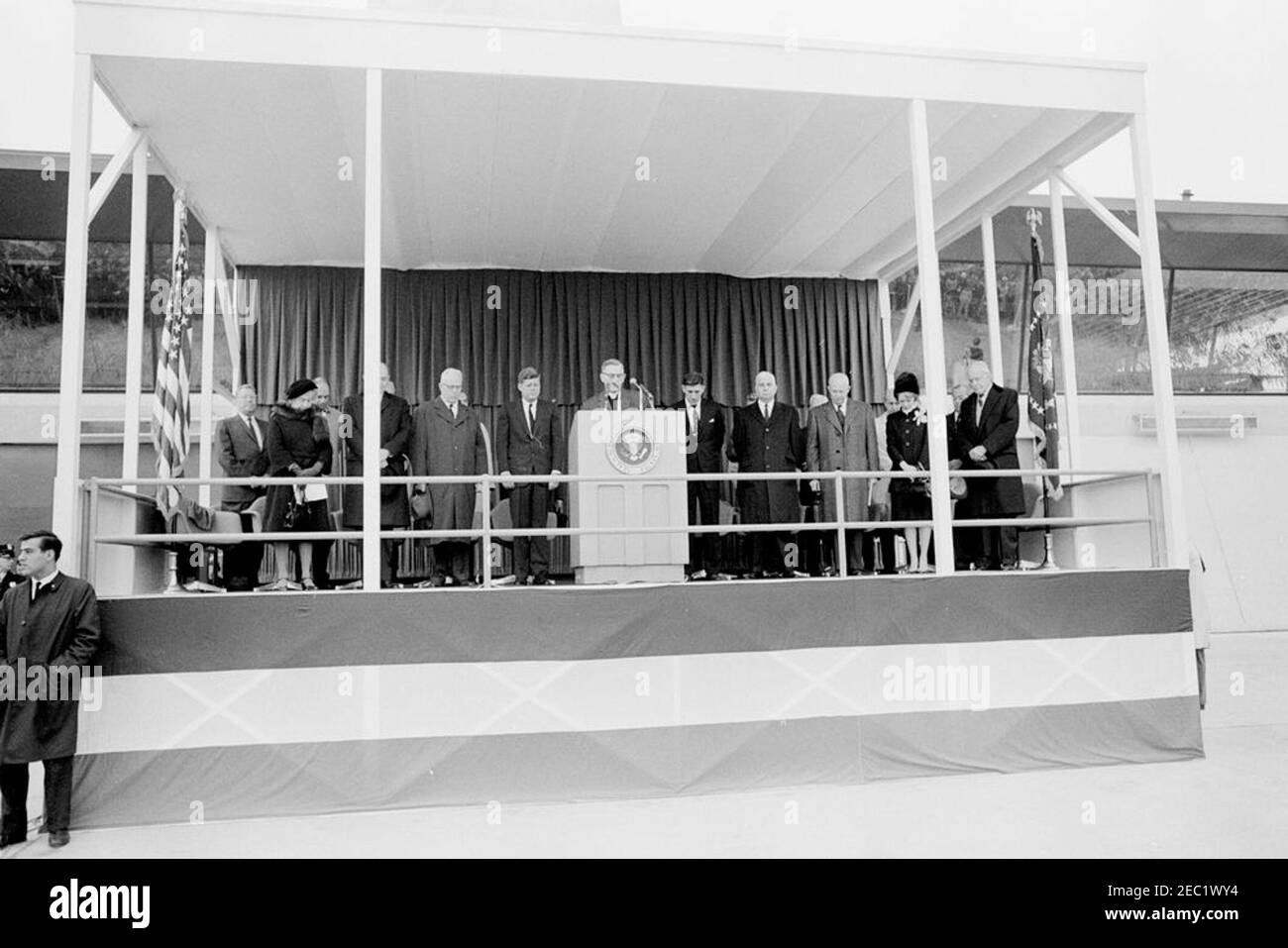 Cerimonie di dedica, aeroporto internazionale di Dulles, 11:12. Cappellano del Senato degli Stati Uniti, il reverendo Frederick Brown Harris (al leggio), effettua l'invocazione alla cerimonia di dedicazione per l'aeroporto internazionale di Dulles, che prende il nome dal defunto Segretario di Stato, John Foster Dulles; il presidente John F. Kennedy si trova a sinistra del leggio. In piedi sulla piattaforma speakersu2019 (L-R): Ex amministratore dell'Agenzia federale dell'aviazione (FAA), generale Elwood R. u201cPeteu201d Quesada; Janet Avery Dulles (vedova dell'ex segretario Dulles); non identificato; Segretario di Stato, Dean Rusk (per lo più hidde Foto Stock