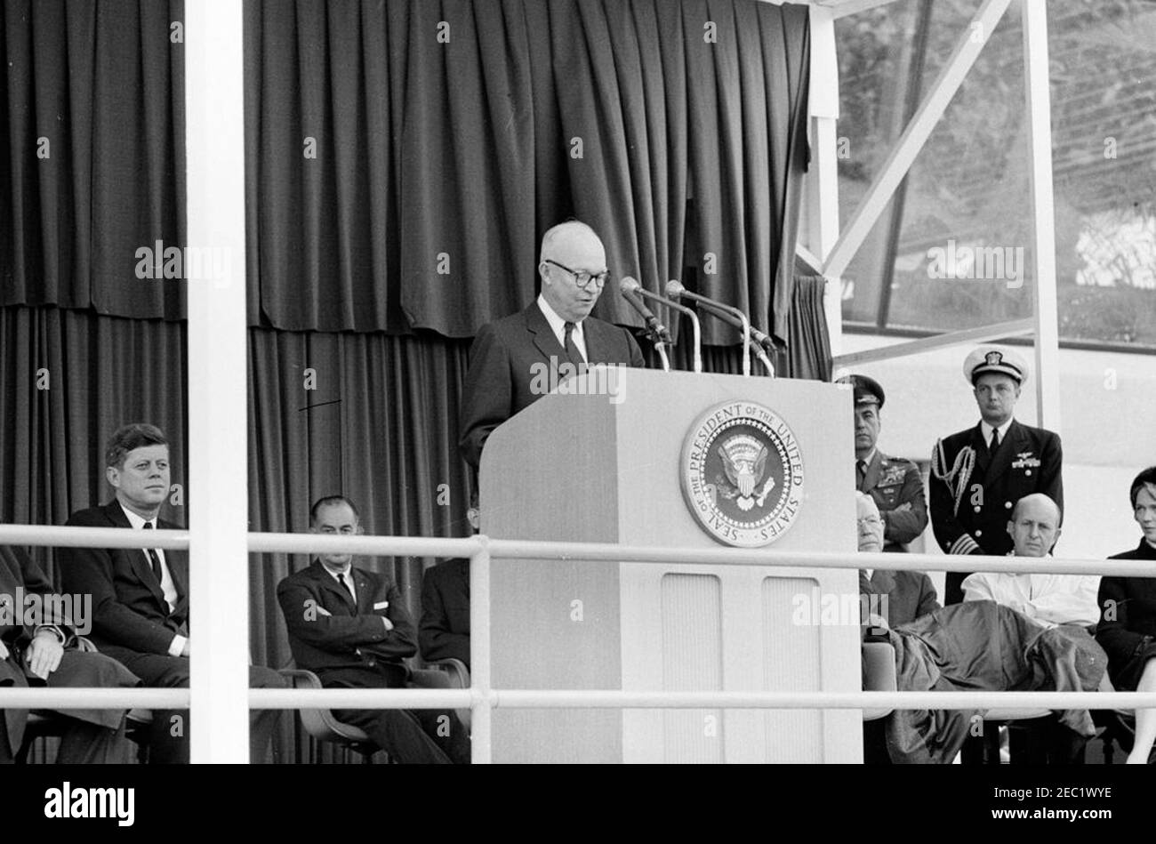 Cerimonie di dedica, aeroporto internazionale di Dulles, 11:12. Eisenhower, ex presidente, Dwight D. Eisenhower (al leggio), commenta la cerimonia di dedica all'aeroporto internazionale di Dulles, che prende il nome dal defunto Segretario di Stato John Foster Dulles; il presidente John F. Kennedy siede a sinistra del leggio. Anche nella foto della piattaforma speakersu2019: Direttore del Bureau of National Capital airports, G. Ward Hobbs (volto oscurato); direttore della Central Intelligence Agency (CIA), John McCone; Air Force Aide al presidente, Brigadier General Godfrey T. McHugh; Naval Aide al presidente, C. Foto Stock