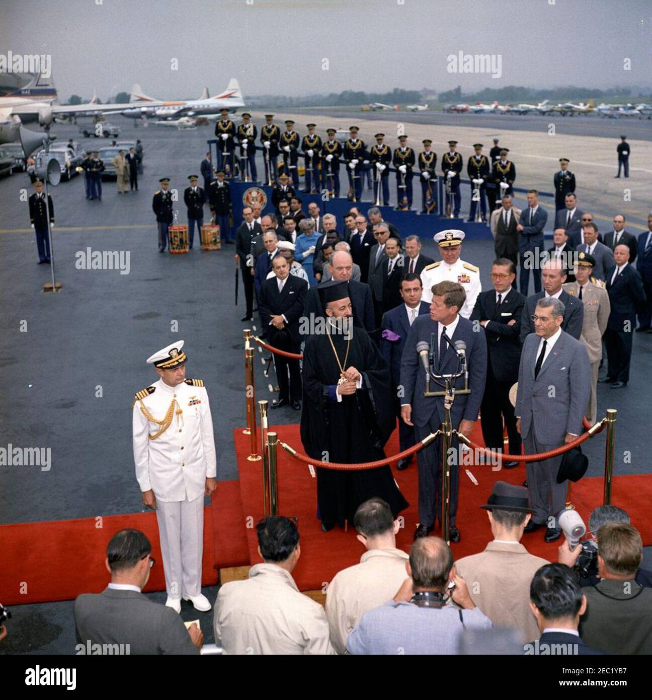 Cerimonia di arrivo dell'Arcivescovo Makarios III, Presidente di Cipro, ore 11. Il presidente John F. Kennedy (ai microfoni) fa le sue osservazioni alle cerimonie di arrivo in onore del presidente della Repubblica di Cipro, l'arcivescovo Makarios III In piedi sulla piattaforma di revisione (L-R): Arcivescovo Makarios III; Segretario di Stato degli Stati Uniti, Dean Rusk; Ministro degli Affari Esteri della Repubblica di Cipro, Spyros Kyprianou; Presidente Kennedy; Capo delle operazioni Navali, Ammiraglio George W. Anderson, Jr. (U.S.N.); Ambasciatore degli Stati Uniti a Cipro, Fraser Wilkins; Capo del protocollo degli Stati Uniti, Angier Biddle Duke; E Ambasciatore della Foto Stock