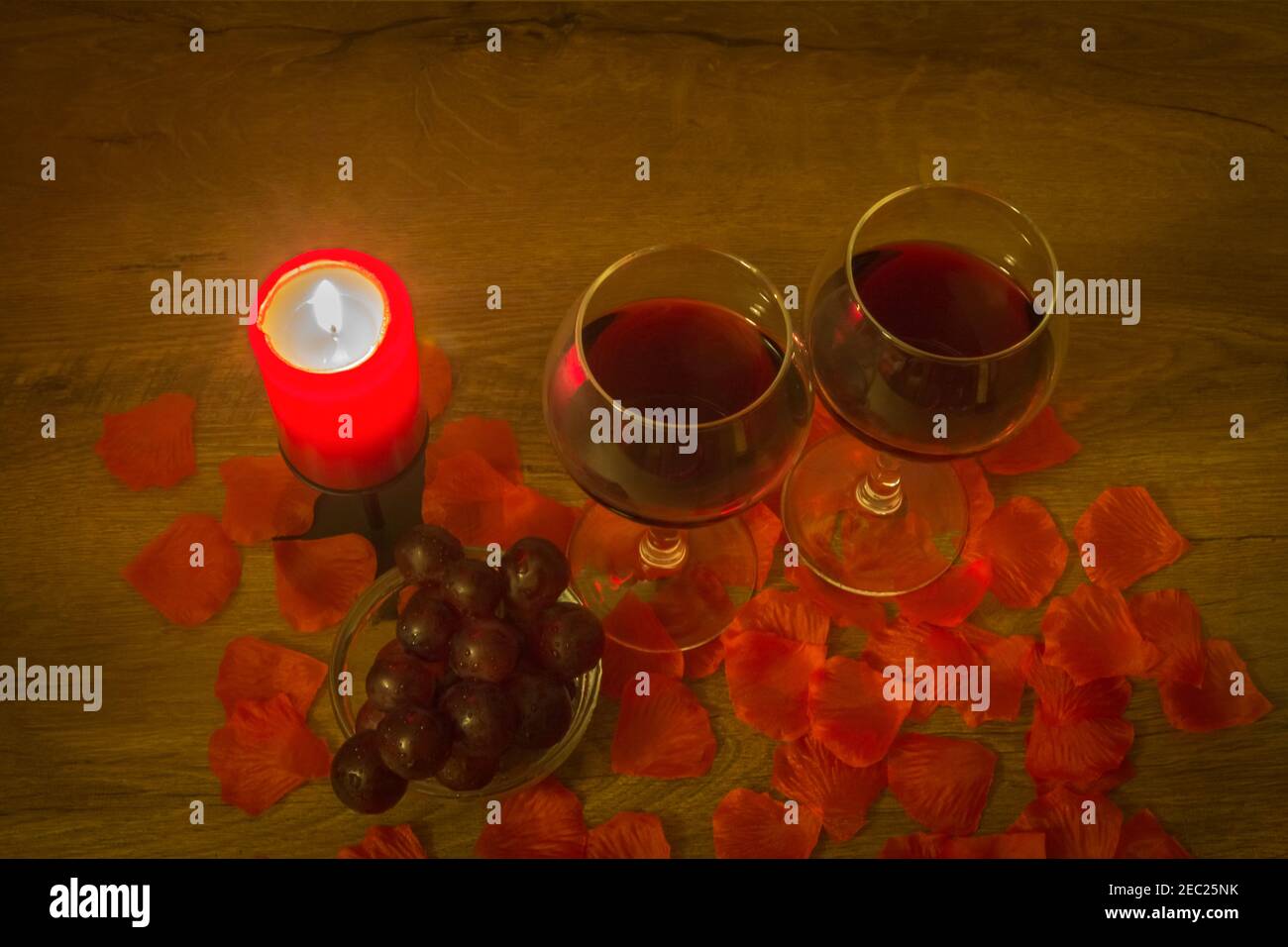 Due bicchieri da vino rosso, uva, candela bruciante e foglie di rosa sul tavolo. Concetto di San Valentino. Foto Stock