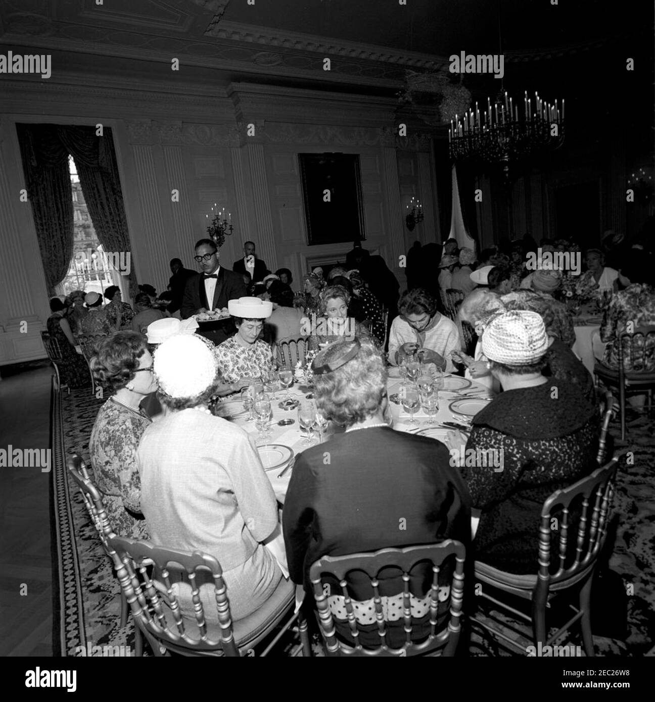 Prima Lady Jacqueline Kennedyu0027s (JBK) pranzo per le mogli Senatorsu0027. Gli ospiti assistono ad un pranzo per le mogli senatorsu2019, dato da First Lady Jacqueline Kennedy nella Sala da pranzo di Stato della Casa Bianca, Washington, D.C. raffigurato sullo sfondo: Frances Marion Grant Bennett (moglie del senatore Wallace Bennett dello Utah); Grace Murphy Dodd (moglie del senatore Thomas Dodd del Connecticut). Foto Stock