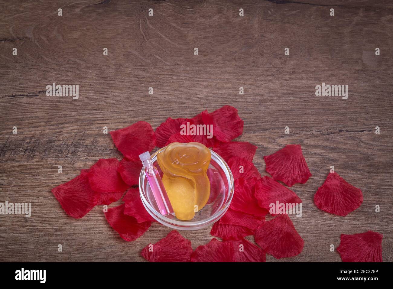Acqua profumata di rosa e fiore di rosa fatto di sapone in vetreria su tavola di legno con petali di rosa. Sfondo per lo spazio di copia. Foto Stock