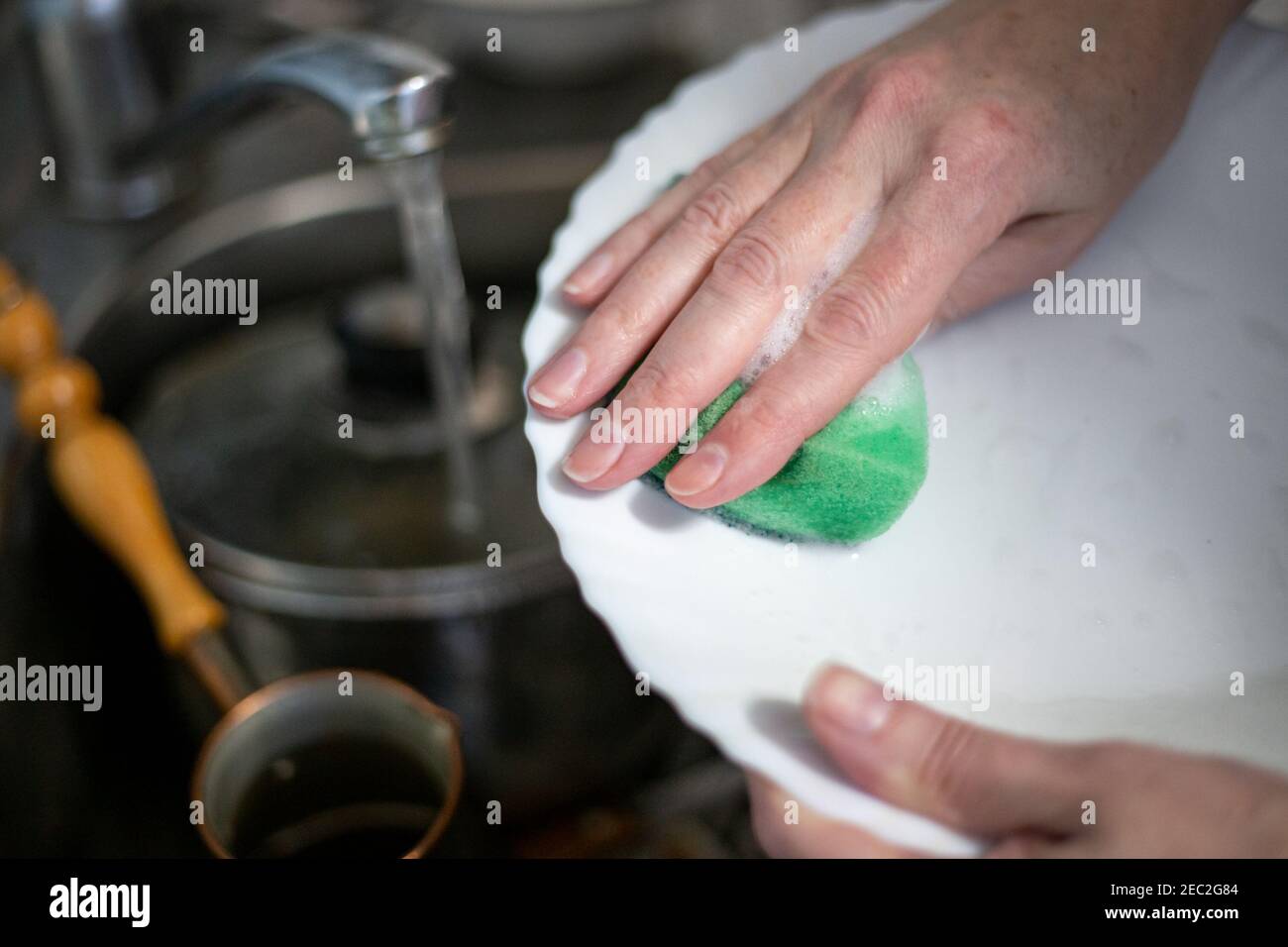 una donna lava i piatti con una spugna di schiuma, tiene un piatto nelle mani sopra il lavandino, l'acqua scorre dal rubinetto Foto Stock