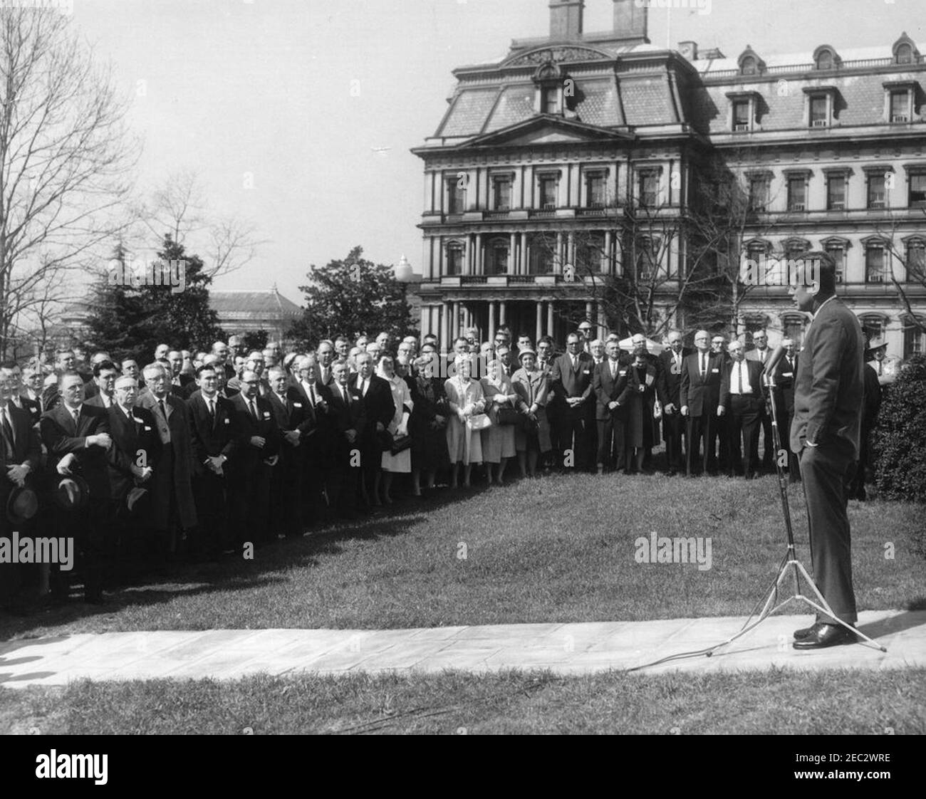 Incontro con i membri della stabilizzazione agricola u0026 Comitati di conservazione, 9:45. Il presidente John F. Kennedy (destra) si rivolge ai membri dei comitati di stabilizzazione e conservazione agricola (ASC) sul prato dell'ala ovest della Casa Bianca, Washington, D.C. l'edificio dell'ufficio esecutivo è visibile sullo sfondo. Foto Stock