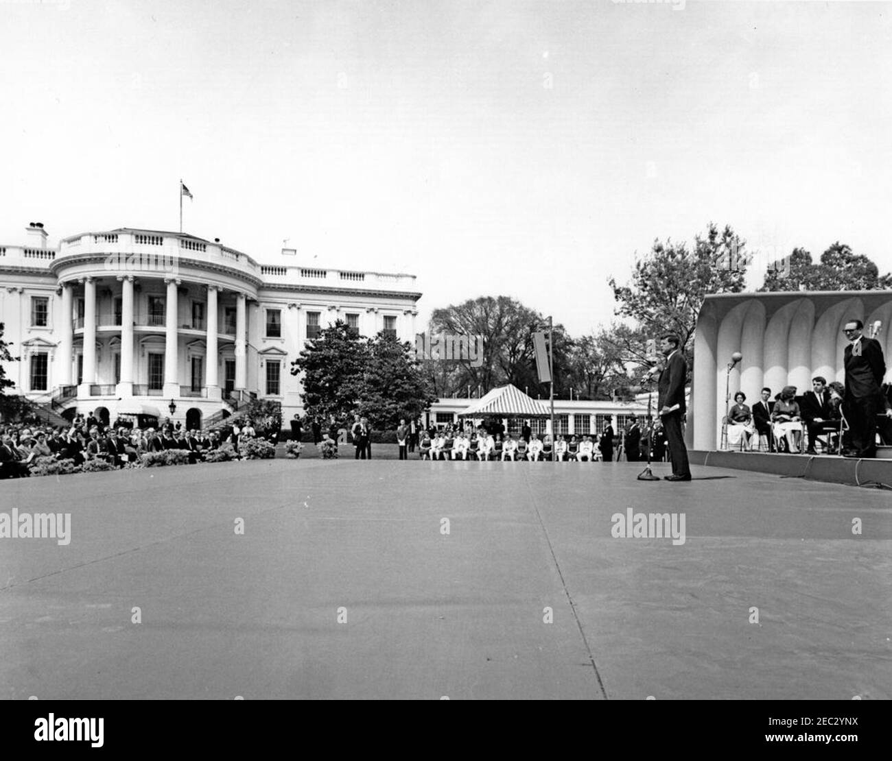 First Lady Jacqueline Kennedyu0027s (JBK) programma musicale per giovani, 14:10. Il presidente John F. Kennedy (a destra) commenta durante un'esibizione della Central Kentucky Youth Symphony Orchestra alla sesta puntata di First Lady Jacqueline Kennedyu2019s Musical Programs for Youth by Youth. Il direttore Joseph Pival si trova a destra; i membri del Berea (Kentucky) College Country Dancer siedono a destra del palco. Il gruppo di danza si è esibito anche in occasione dell'evento che si è tenuto sul South Lawn of the White House, Washington, D.C. Foto Stock