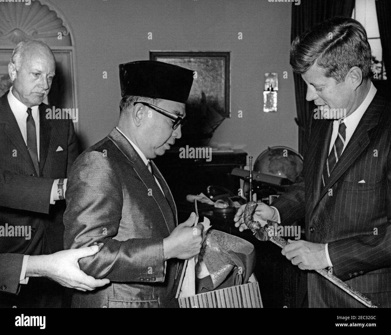 Incontro con Tun Abdul Razak, Vice primo Ministro della Malaya, 11:58. Il presidente John F. Kennedy scambia regali con il vice primo ministro e ministro della Difesa della Malaya, Tun Abdul Razak Hussein (centro sinistra), durante un incontro nell'Ufficio ovale. L'ambasciatore degli Stati Uniti in Malesia, Charles F. Baldwin, si trova all'estrema sinistra. White House, Washington, D.C. [vedi anche MO 74.334a-b, u0022Jeweled kris e sheathu0022] Foto Stock