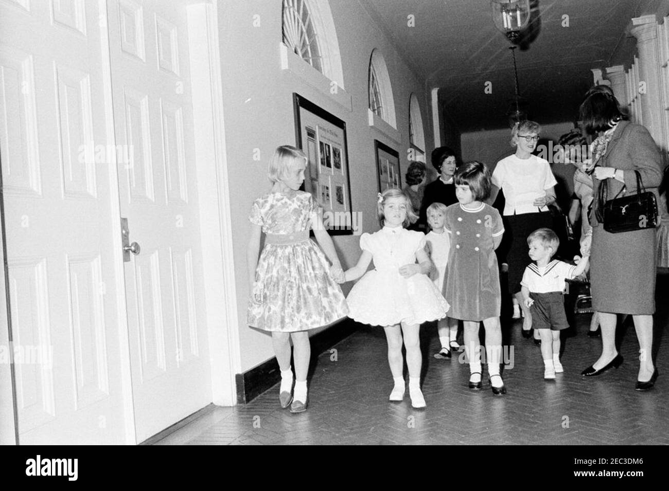 Festa di compleanno per Caroline Kennedy e John F. Kennedy, Jr. Caroline Kennedy tiene le mani con l'amico di famiglia Kennedy, Shawn fragile, mentre cammina nel corridoio dell'ala est della Casa Bianca, Washington, D.C., durante una festa di compleanno congiunta per lei e suo fratello, John F. Kennedy, Jr. Maria Shriver cammina a destra di Caroline; La nonna di Carolineu0027s, Janet Auchincloss, cammina sullo sfondo. Foto Stock