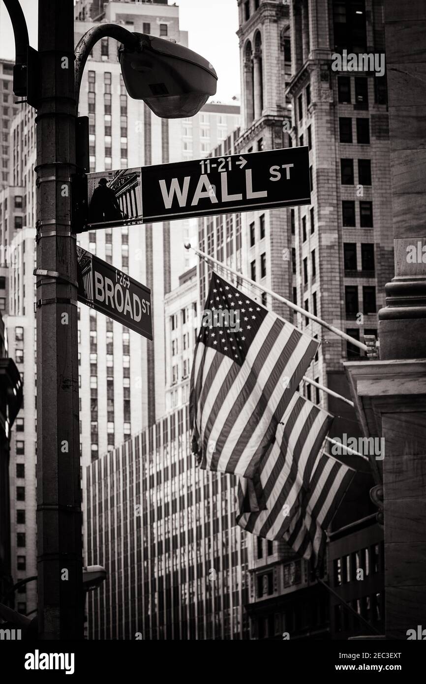 Segno di Wall Street a New York su una strada Lampada con tre bandiere americane e edifici sullo sfondo in bianco e nero Foto Stock