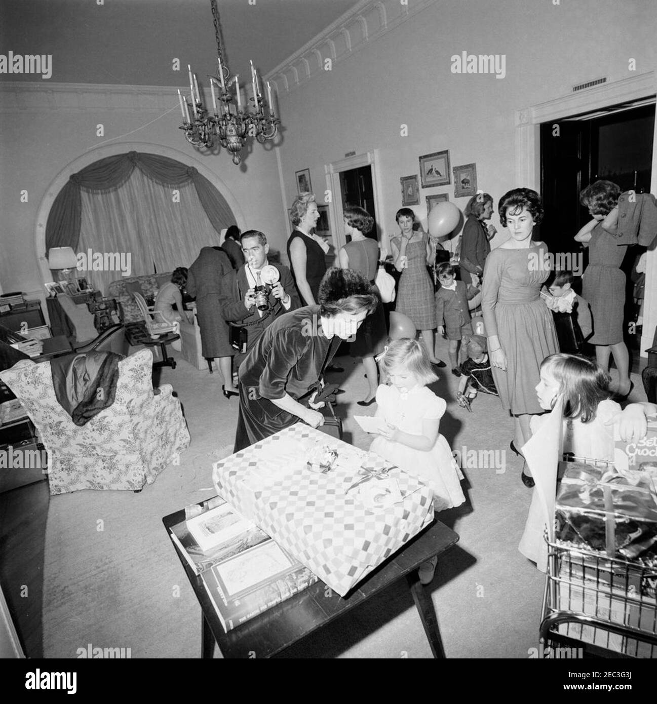 Festa di compleanno per Caroline Kennedy e John F. Kennedy, Jr. Caroline Kennedy visita con sua nonna, Janet Auchincloss, durante una festa di compleanno congiunta per lei e suo fratello, John F. Kennedy, Jr.; diversi regali siedono sul tavolo in primo piano. Anche nella foto: Primo segretario sociale Ladyu0027s, Letizia Baldrige; fotografo della Casa Bianca, capo Robert L. Knudsen. West sitting Hall, White House, Washington, D.C. [i graffi nella parte superiore sinistra dell'immagine sono originali al negativo.] Foto Stock