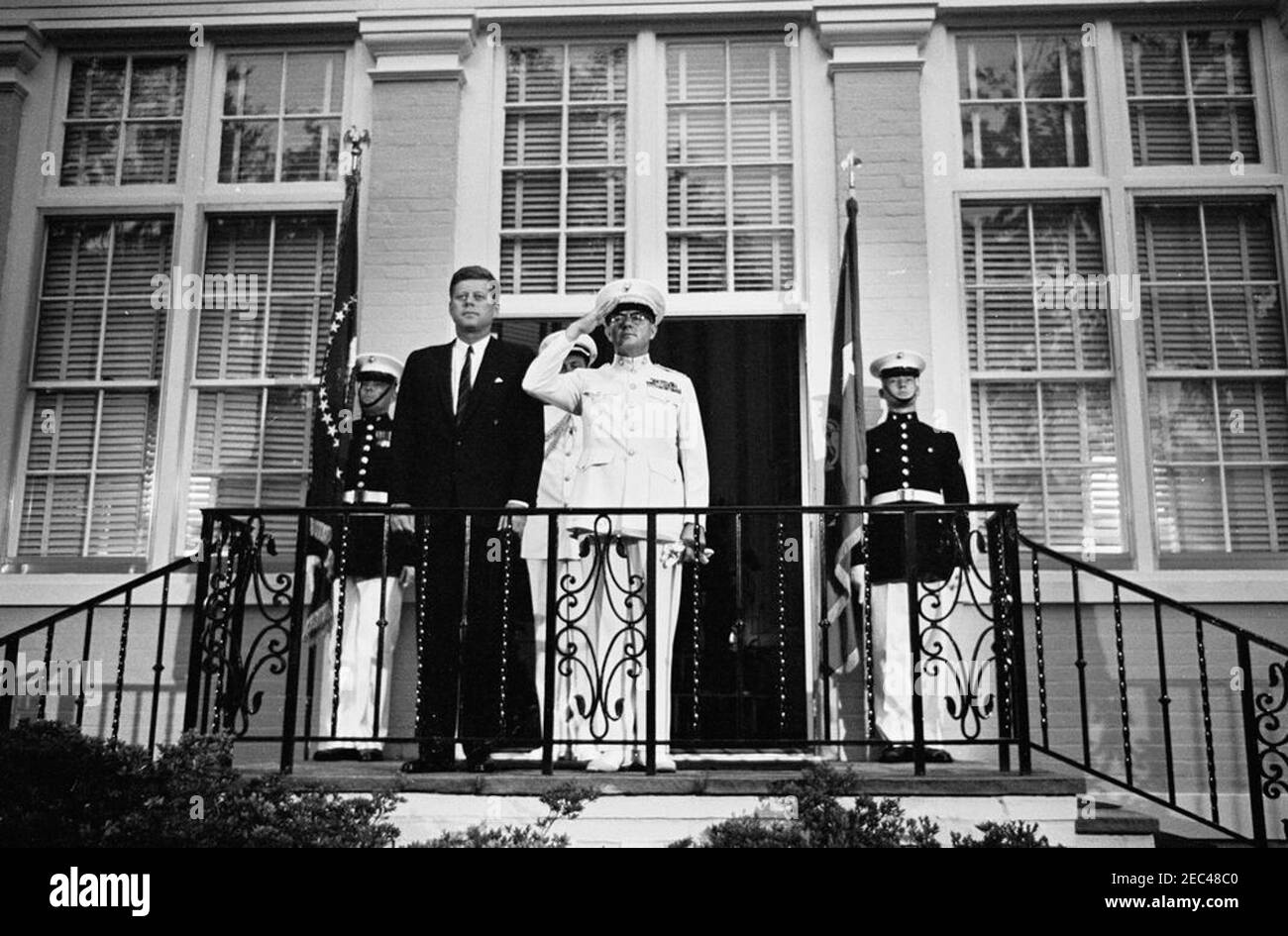 Il Presidente Kennedy vede la Marine Corpsu0027 Evening Parade, presso le Marine Barracks Washington, D.C. (8th u0026 i Streets, se), alle 21.00. Il presidente John F. Kennedy si trova con il comandante del corpo dei Marine degli Stati Uniti, il generale David M. Shoup (in saluto), di fronte alla Casa Commandantu2019s presso le Marine Barracks (u201c8th u0026 Iu201d) a Washington, D.C. Naval Aide al presidente, Capitano Tazewell Shepard (per lo più nascosto), si trova dietro il generale Shoup; I Marines che fiancheggiano la porta non sono identificati. Foto Stock