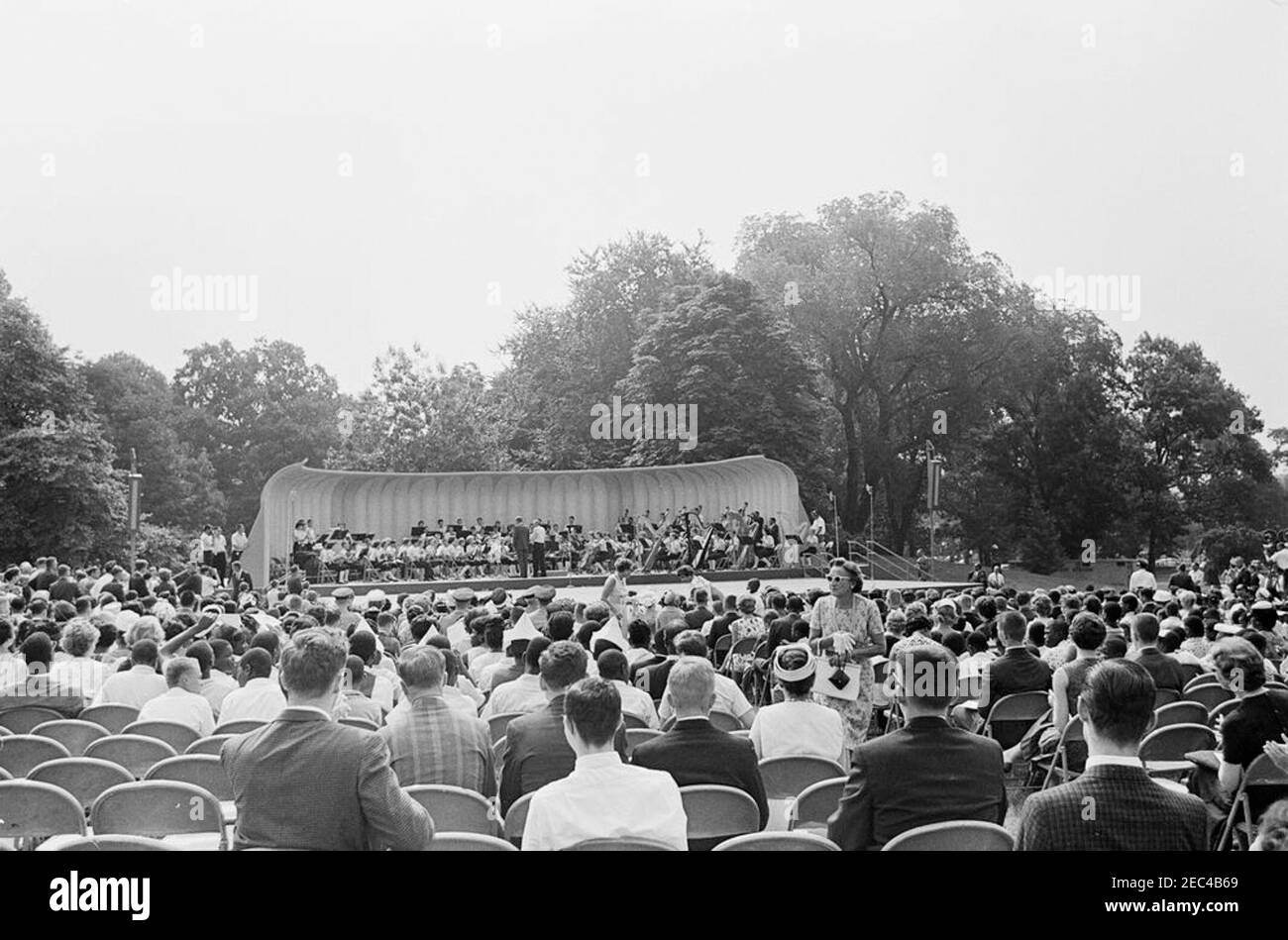 First Lady Jacqueline Kennedyu0027s (JBK) programma musicale per la gioventù, 10:35. Il presidente John F. Kennedy (centro a sinistra, in background, con ritorno alla macchina fotografica) visita con i membri della National High School Symphony Orchestra del National Music Camp di Interlochen, Michigan, durante la quarta serie della First Lady Jacqueline Kennedyu0027s di programmi musicali per la gioventù; Il presidente Kennedy ha espresso osservazioni per l’occasione. Direttore d'orchestra e presidente del National Music Camp, il Dr. Joseph E. Maddy (in tribuna), si trova a destra del presidente. South Lawn, Casa Bianca, Washington Foto Stock