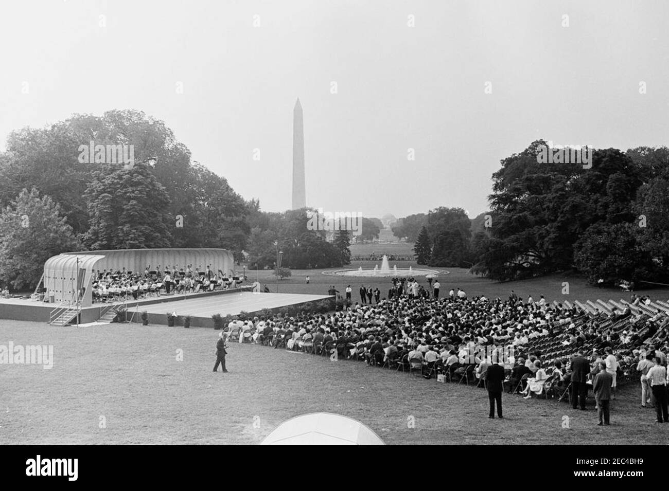 First Lady Jacqueline Kennedyu0027s (JBK) programma musicale per la gioventù, 10:35. Ampia vista del Prato Sud durante la quarta in prima Lady Jacqueline Kennedyu2019s serie di programmi musicali per la Gioventù. I membri della National High School Symphony Orchestra del National Music Camp di Interlochen, Michigan, si esibiscono a sinistra in background; il presidente del National Music Camp, Dr. Joseph E. Maddy (in tribuna), dirige l'orchestra. Il Washington Monument e il Jefferson Memorial sono visibili in lontananza. White House, Washington, D.C. Foto Stock