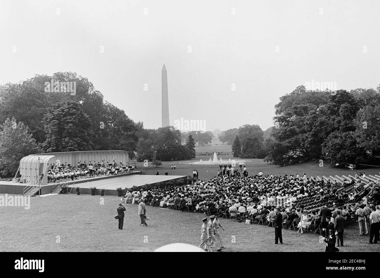 First Lady Jacqueline Kennedyu0027s (JBK) programma musicale per la gioventù, 10:35. Ampia vista del Prato Sud durante la quarta in prima Lady Jacqueline Kennedyu2019s serie di programmi musicali per la Gioventù. I membri della National High School Symphony Orchestra del National Music Camp di Interlochen, Michigan, si esibiscono a sinistra in background; il presidente del National Music Camp, Dr. Joseph E. Maddy (in tribuna), dirige l'orchestra. National Park Service (NPS) fotografo, Abbie Rowe (centro a sinistra), cammina in primo piano. Il Washington Monument e il Jefferson Memorial sono visibili Foto Stock