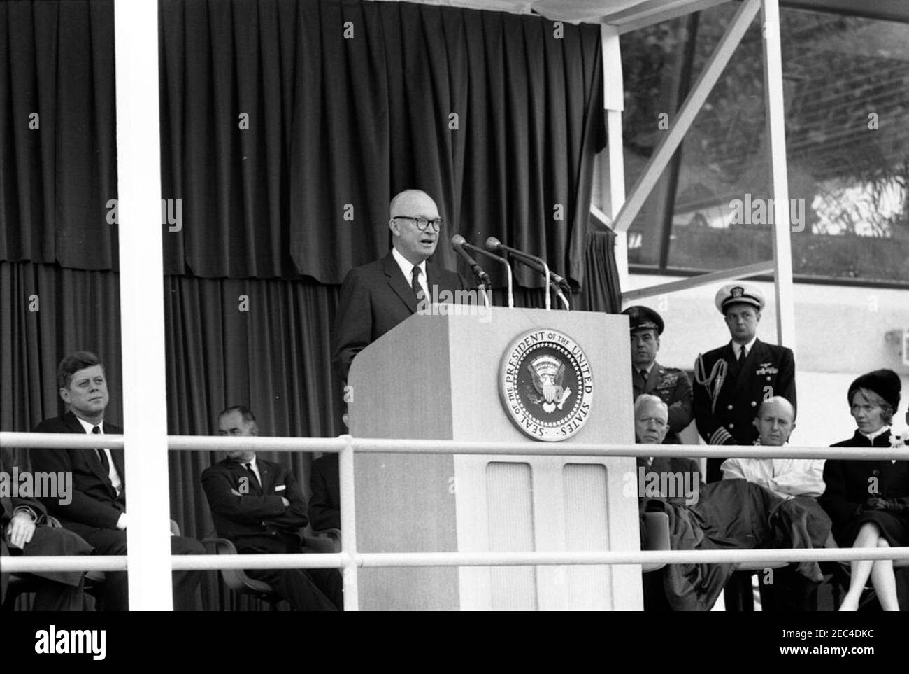 Cerimonie di dedica, aeroporto internazionale di Dulles, 11:12. Eisenhower, ex presidente Dwight D. Eisenhower (al leggio), commenta la cerimonia di dedica all'aeroporto internazionale di Dulles, che prende il nome dal defunto Segretario di Stato John Foster Dulles; il presidente John F. Kennedy siede a sinistra. Anche nella foto della piattaforma speakersu2019: Direttore del Bureau of National Capital airports, G. Ward Hobbs (volto oscurato); direttore della Central Intelligence Agency (CIA), John McCone; Air Force Aide al presidente, Brigadier General Godfrey T. McHugh; Naval Aide al presidente, Captain T. Foto Stock