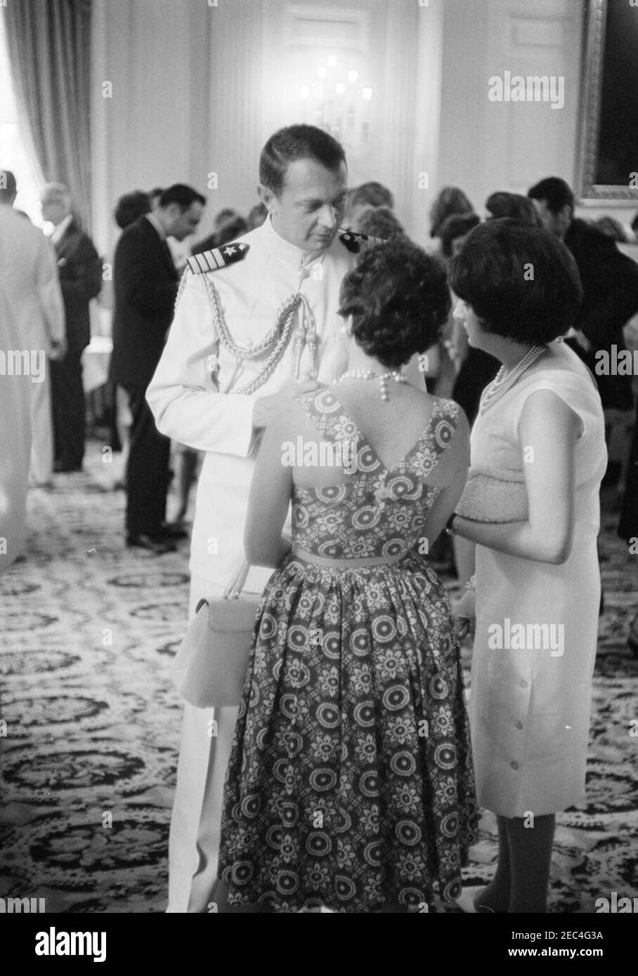 Accoglienza militare alla Casa Bianca, alle 18:00. Naval Aide al presidente, Captain Tazewell Shepard, visita con la Casa Bianca corrispondente per United Press International (UPI), Helen Thomas (a destra), e una donna non identificata (centro, di nuovo alla telecamera) ad un ricevimento militare. State Dining Room, White House, Washington, D.C. Foto Stock