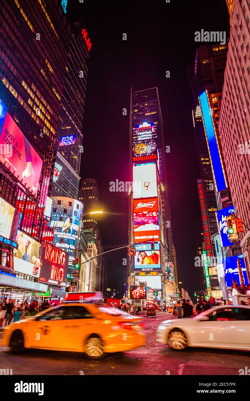 Una vista notturna di Times Square, la più famosa attrazione turistica del mondo, guardando a nord con un taxi sfocato e un'auto che passa Foto Stock