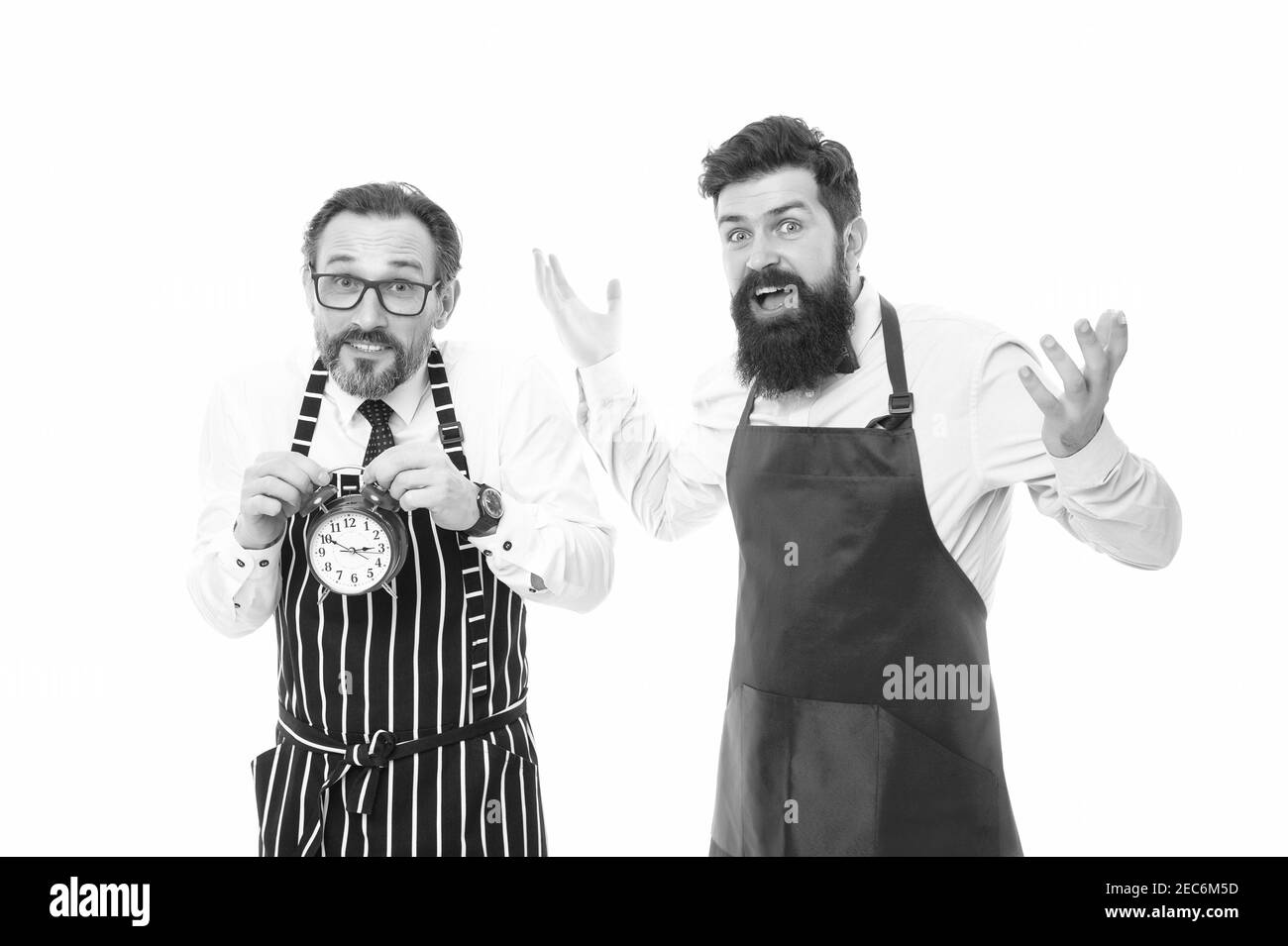 Uomo sopportato hipster e cuoco maturo grembiule sfondo bianco. Orari di lavoro e pausa pranzo. Mancanza di tempo. Controllare l'ora. È ora di pranzo. Cucina maschile con sveglia. Scadenza non riuscita. Foto Stock