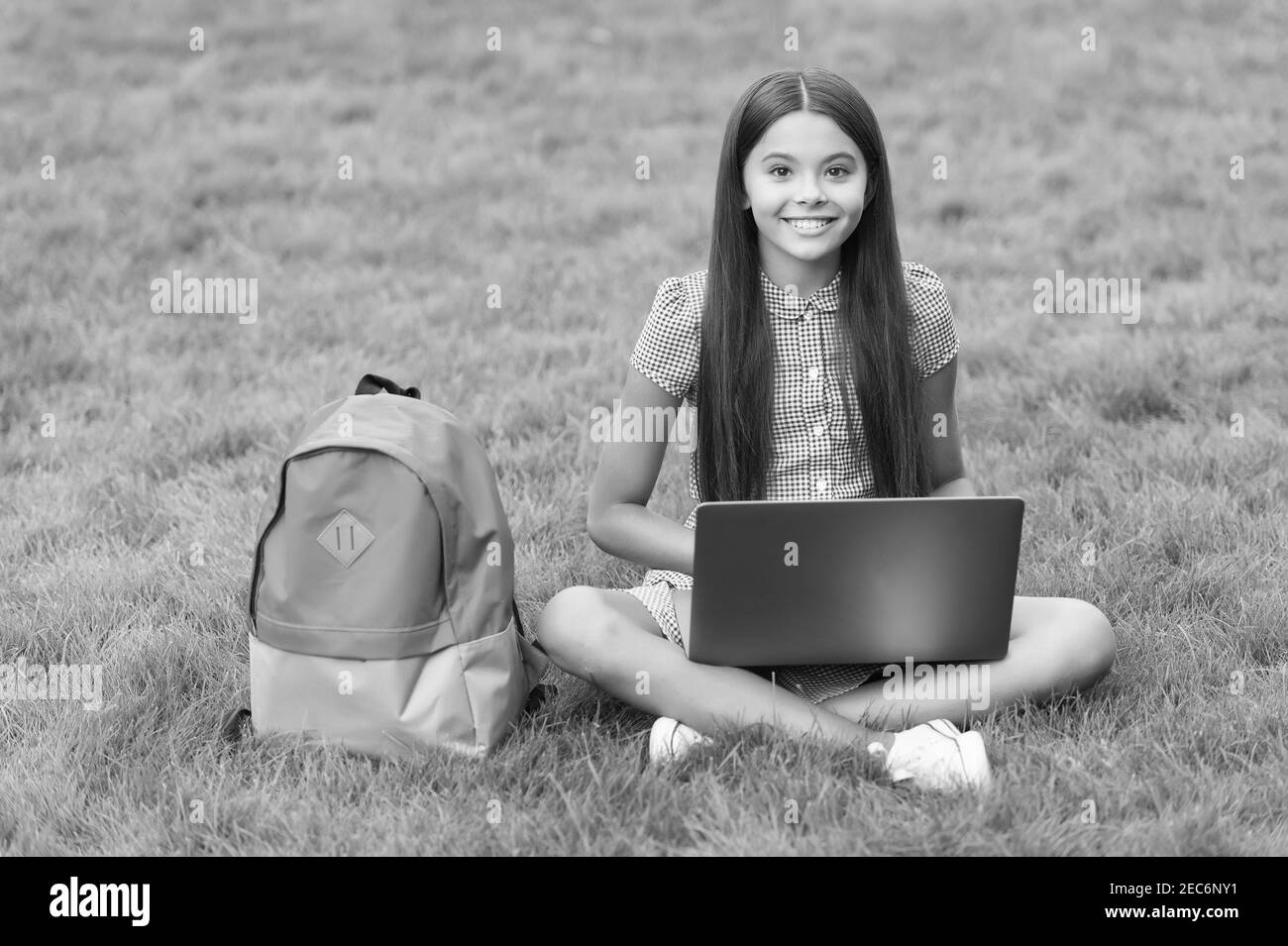 la ragazza reagisce mentre si usa un computer portatile sedersi su erba verde nel parco con la scuola indietro, istruzione. Foto Stock