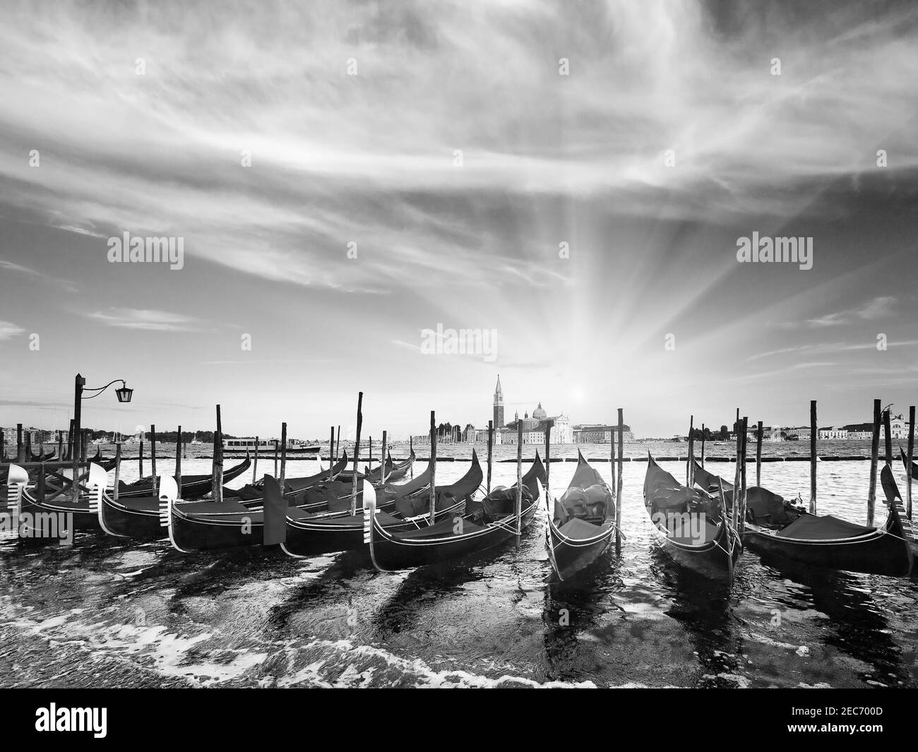 Scala di grigi. Gondole parcheggiate su Piazza San Marco e l'argine del Palazzo Ducale e il sole del tramonto (Venezia, Italia). Foto Stock