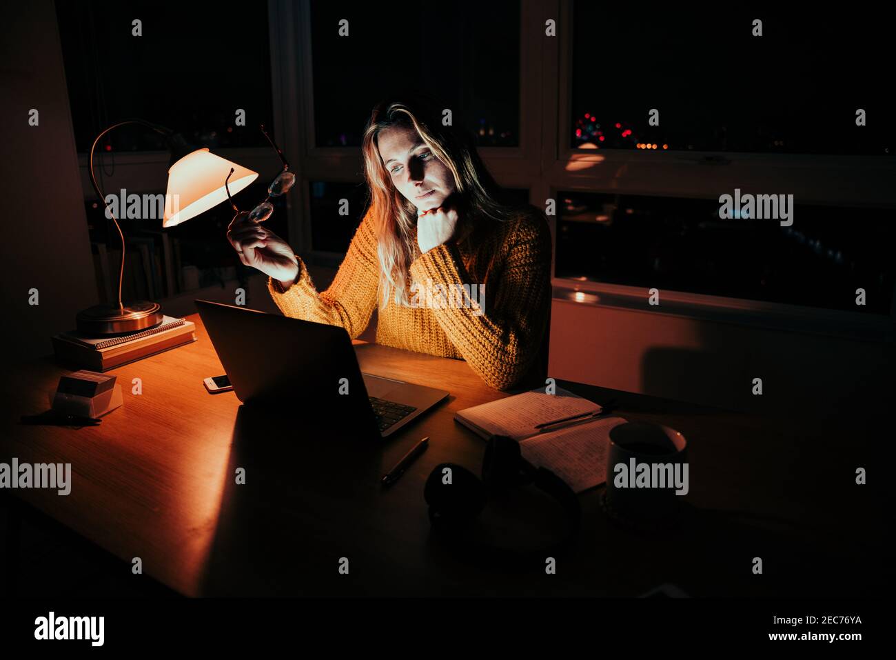 Donna caucasica di affari che tiene gli occhiali che lavorano tardi alla lettura di notte articolo online in ufficio domestico Foto Stock