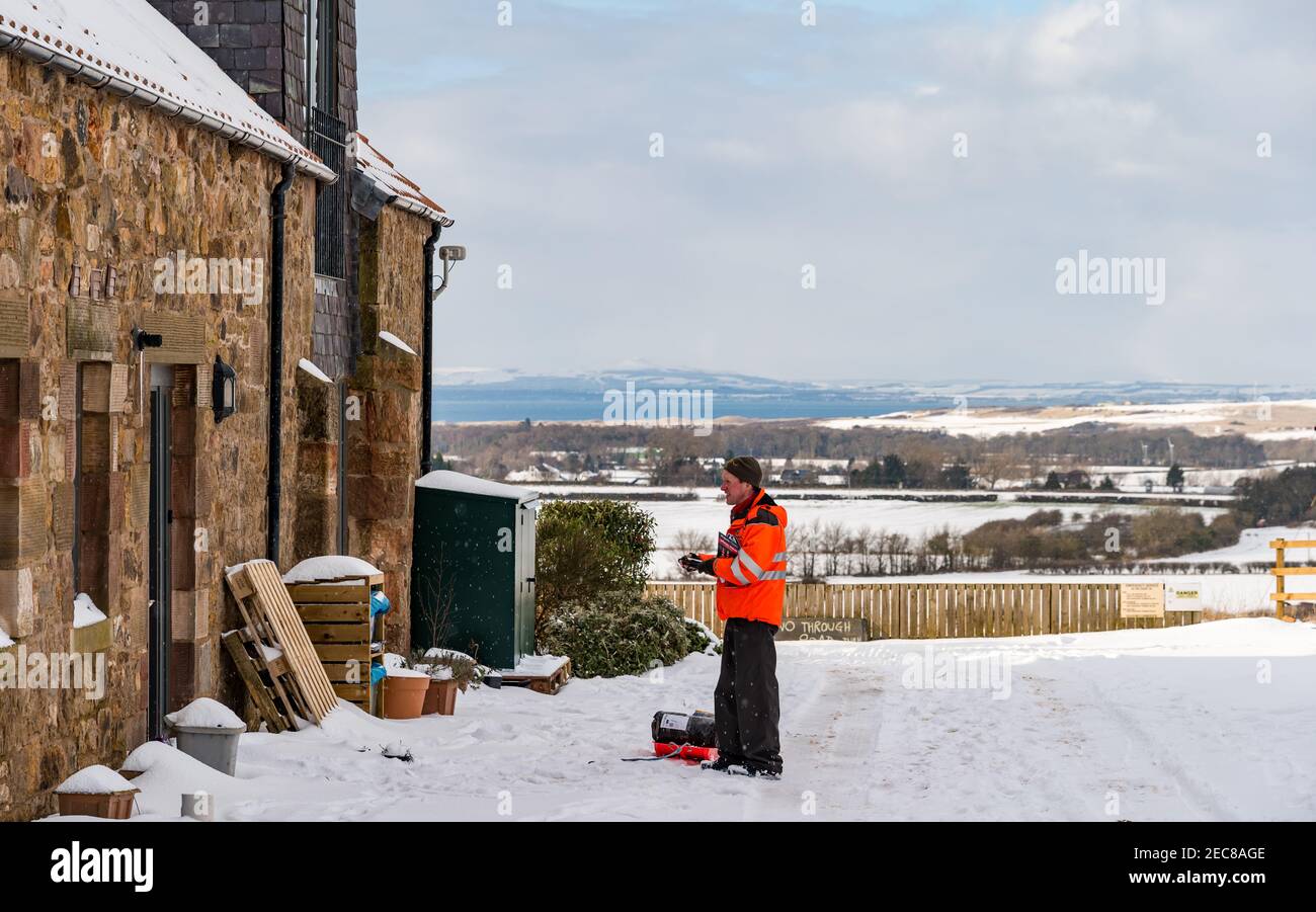 Il postino della Royal Mail che consegna pacchi e lettere nel posto usando una slitta nella neve, East Lothian, Scozia, Regno Unito Foto Stock