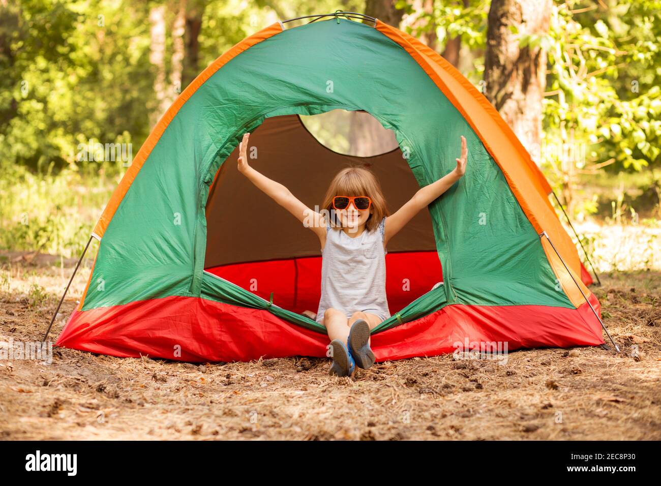 felice bambina in tenda da campeggio godetevi le vacanze nella foresta con le mani in su. Foto Stock