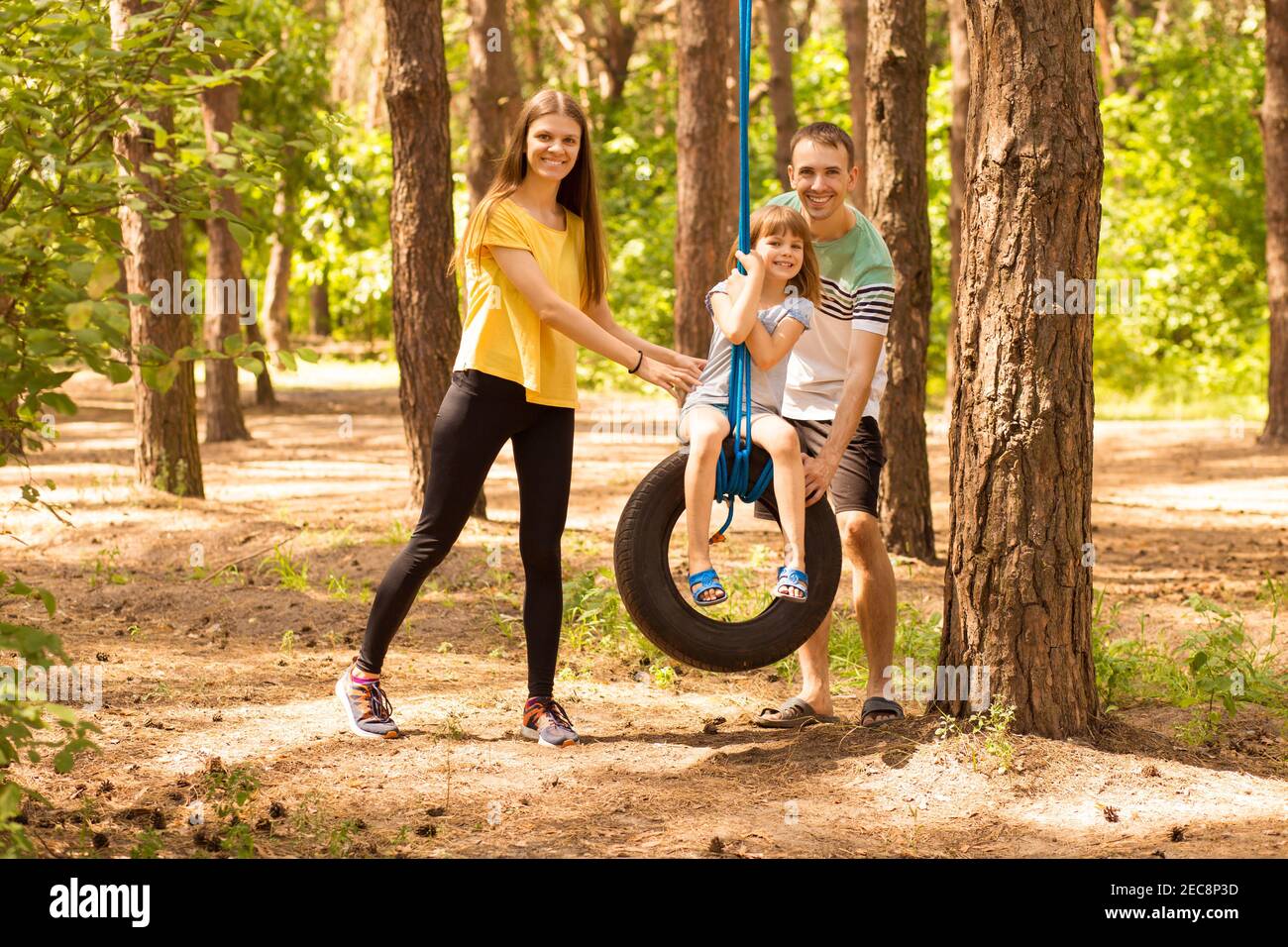 ritratto di giovane genitore felice che ruota figlia su ruota, con la natura estiva sullo sfondo Foto Stock