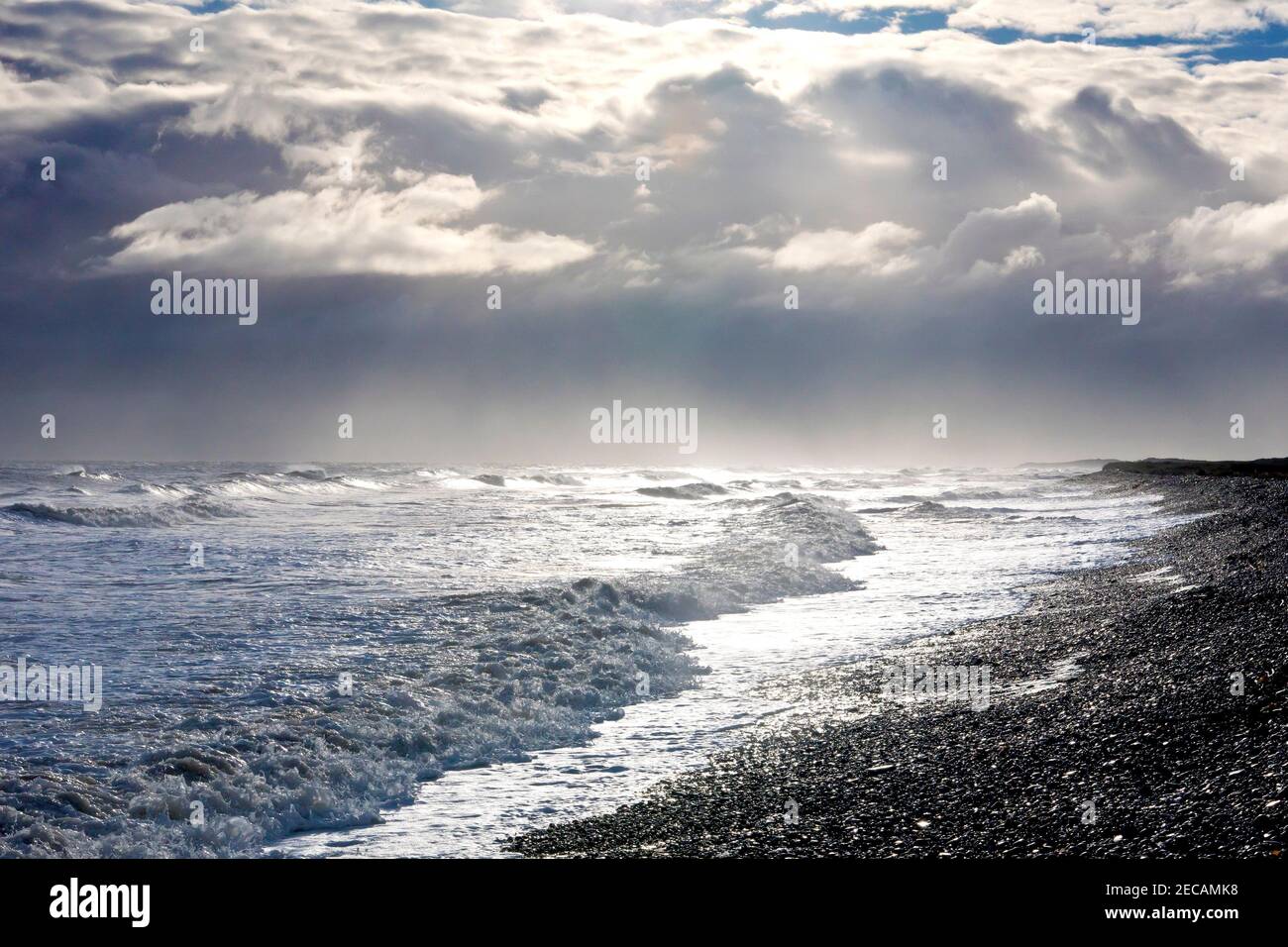 Un'onda si rompe e corre a riva sulla spiaggia di ghiaia di Arbroath, di nuovo illuminata da un sole basso in una giornata ventosa e tempestosa. Foto Stock