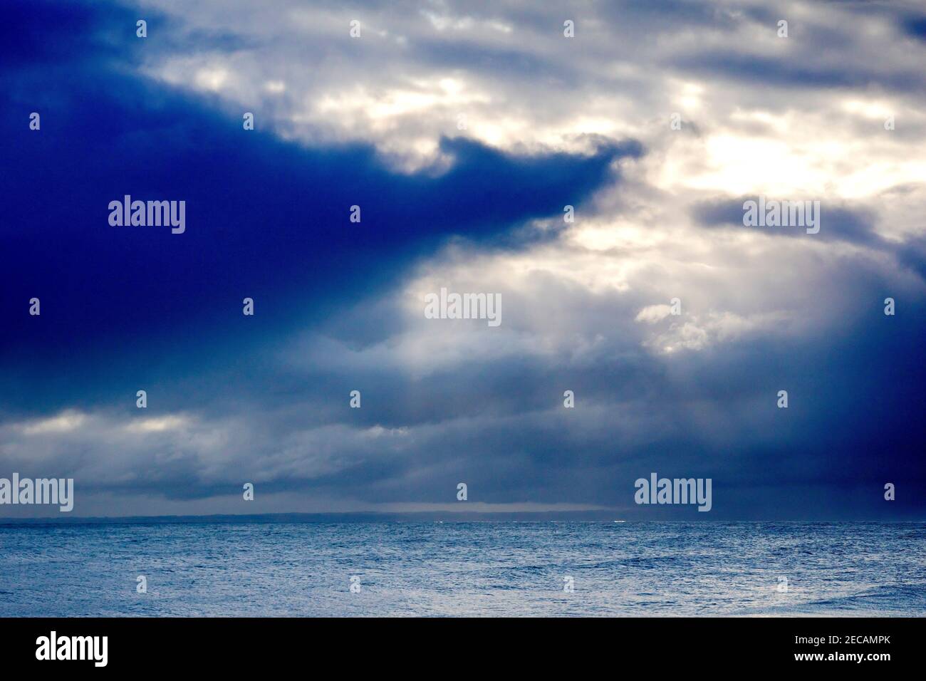 Una rottura nelle nuvole di pioggia permette al sole di mandare giù alcuni alberi deboli di luce per illuminare il mare. Foto Stock