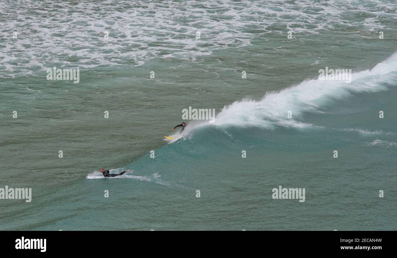 Surfers cattura un'onda al largo della spiaggia di Porthcurno, Penwith Peninsula, Cornovaglia Foto Stock