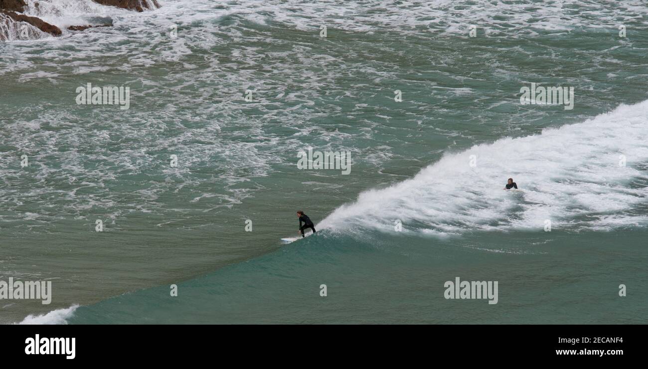 Surfers cattura un'onda al largo della spiaggia di Porthcurno, Penwith Peninsula, Cornovaglia Foto Stock