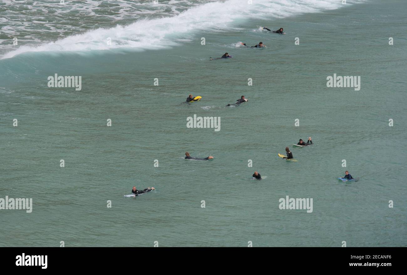 Surfers in attesa di un'onda al largo della spiaggia di Porthcurno, Penwith Peninsula, Cornovaglia Foto Stock