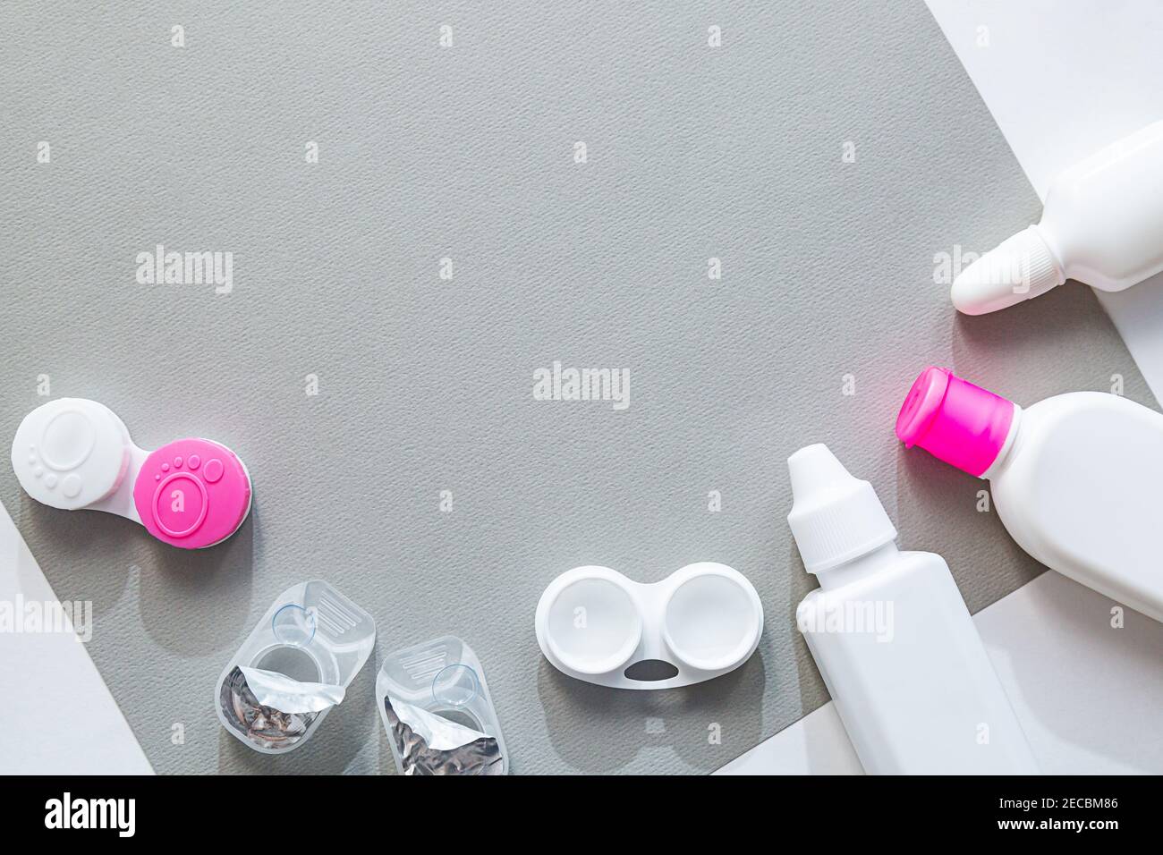 Le lenti a contatto e gli accessori sono piatti su uno sfondo grigio. Composizione con flaconi di soluzione e contenitori di lenti con spazio di copia Foto Stock