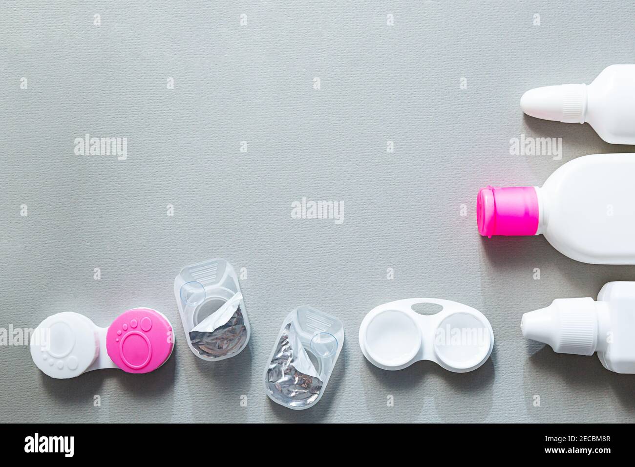 Le lenti a contatto e gli accessori sono piatti su uno sfondo grigio. Composizione con flaconi di soluzione e contenitori di lenti con spazio di copia Foto Stock