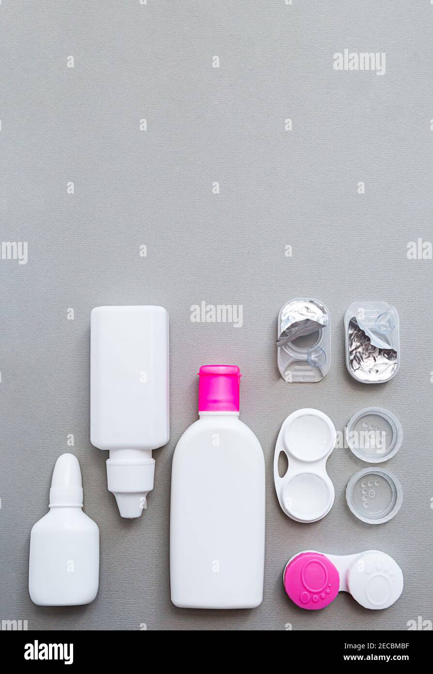 Le lenti a contatto e gli accessori sono piatti su uno sfondo grigio. Composizione con flaconi di soluzione e contenitori di lenti con spazio di copia Foto Stock