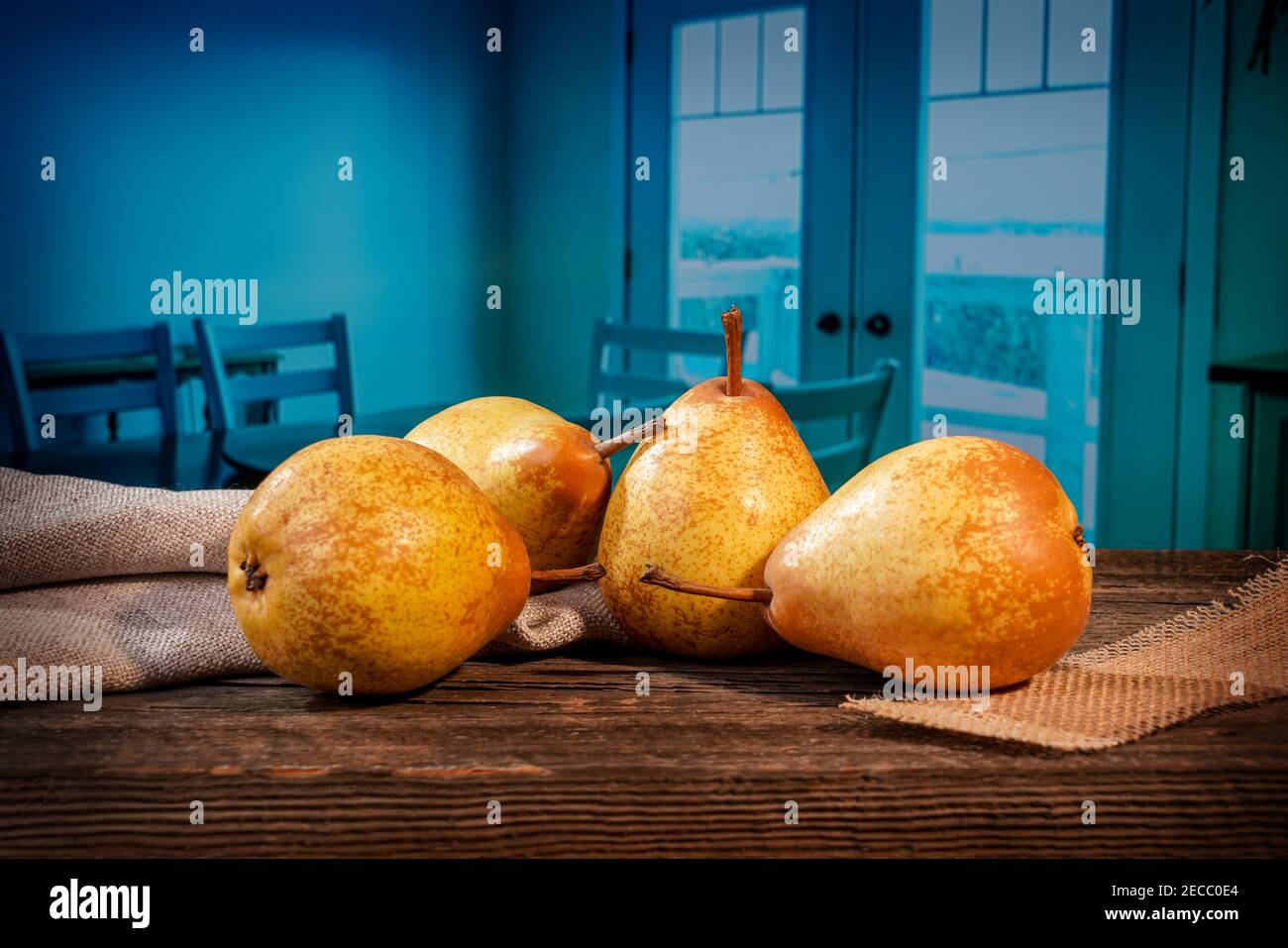 Quattro pere gialle e una felce su un bosco di fienile tavolo davanti ad una sala da pranzo blu Foto Stock