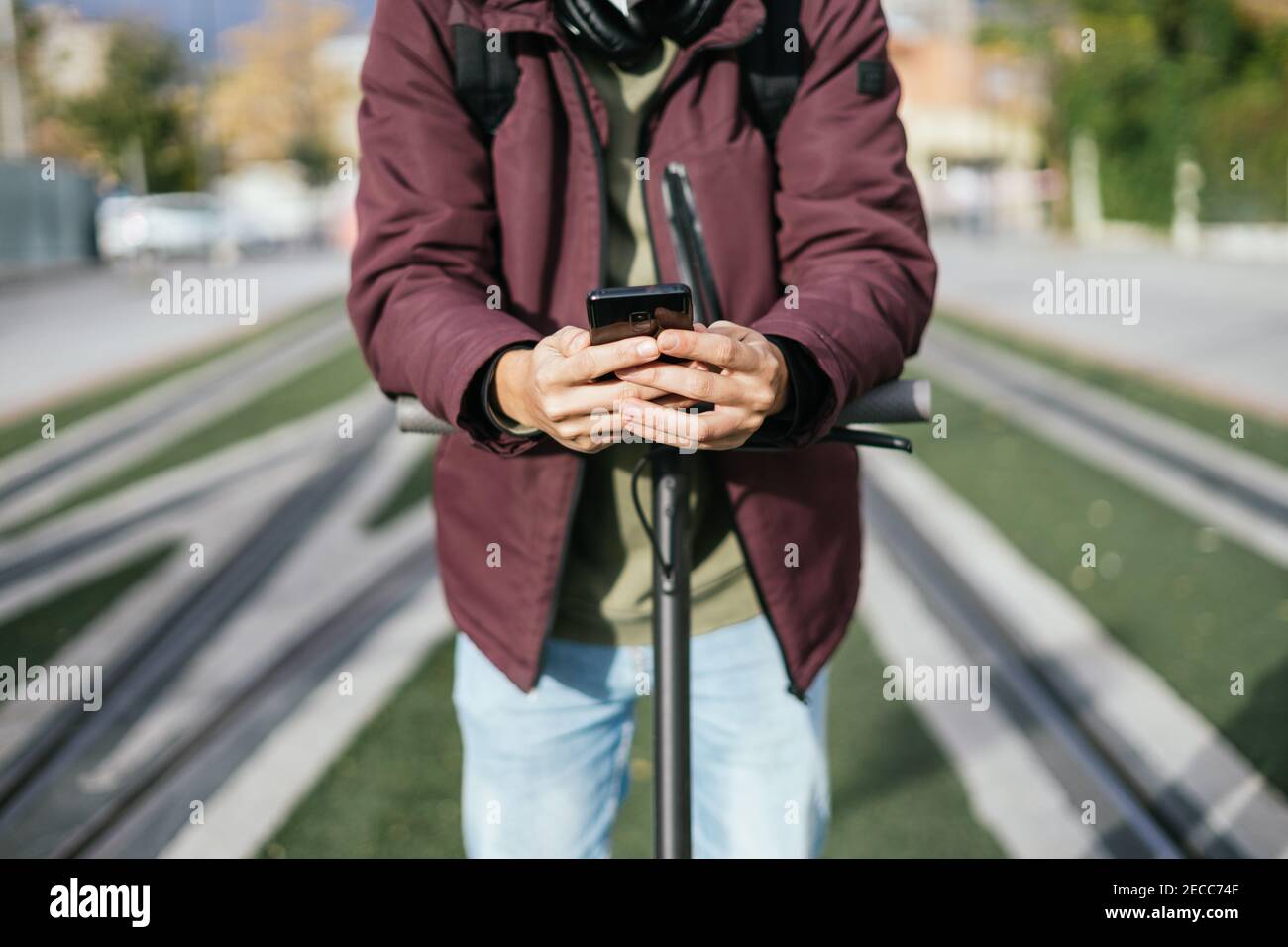 Mani di uno studente che invia un messaggio con il suo cellulare sullo scooter elettrico. Foto Stock