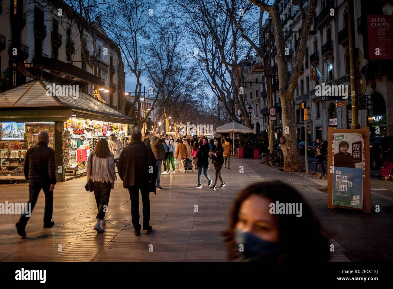 Barcellona, Spagna. 13 febbraio 2021, Barcellona, Catalogna, Spagna: In questo sabato sera la gente cammina lungo la Rambla di Barcellona accanto a un poster della campagna elettorale (che mostra Carles Puigdemon di Junts per il partito Catalunya) durante il giorno di silenzio elettorale. Domenica la Catalogna si dirige alle elezioni regionali in mezzo alla crisi pandemica del coronavirus e a un conflitto che ha portato politici pro-indipendenza in carcere e in esilio durante l'ultima legislatura. Credit: Jordi Boixareu/Alamy Live News Foto Stock